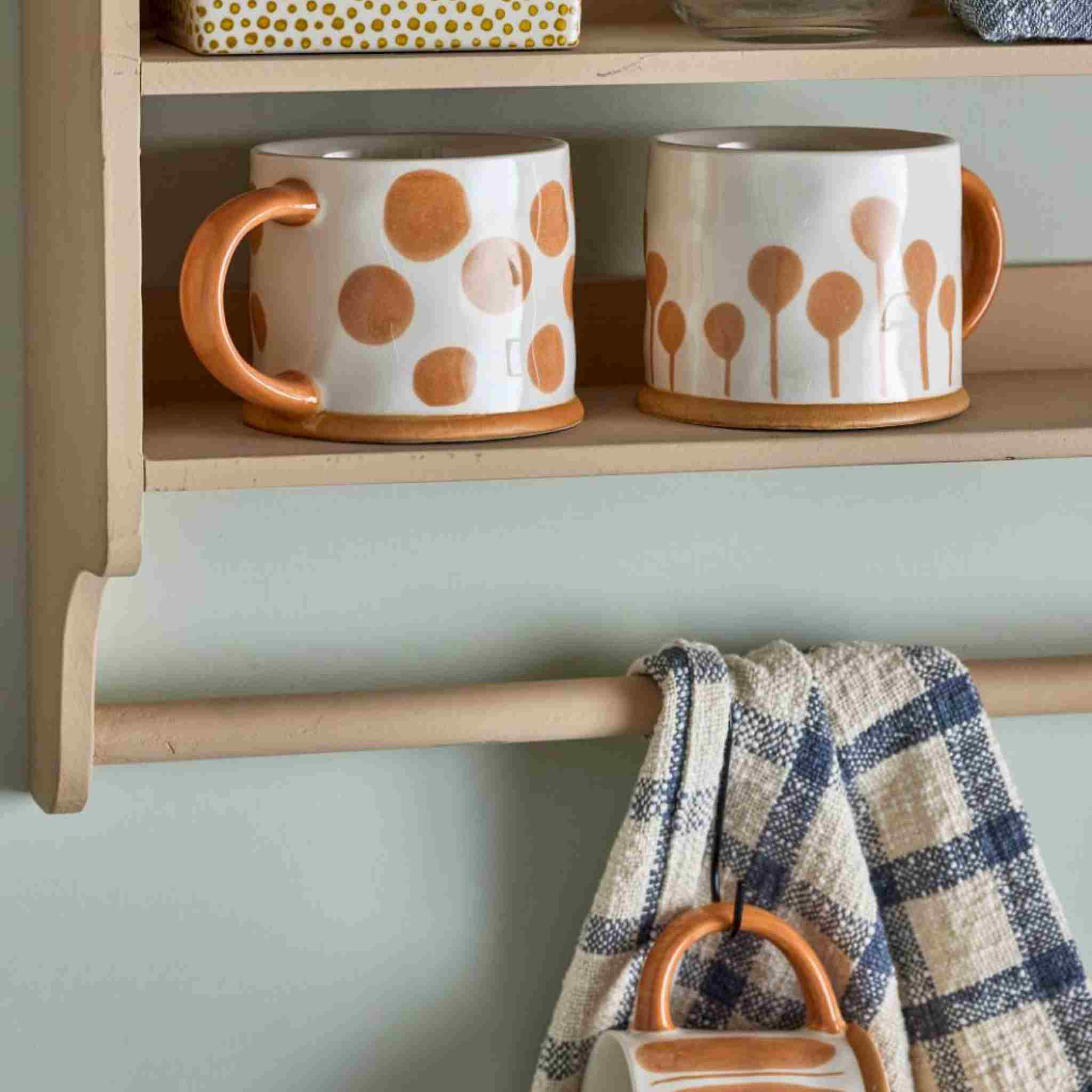 Two mugs with polka dot designs on a wooden shelf against a light green wall.