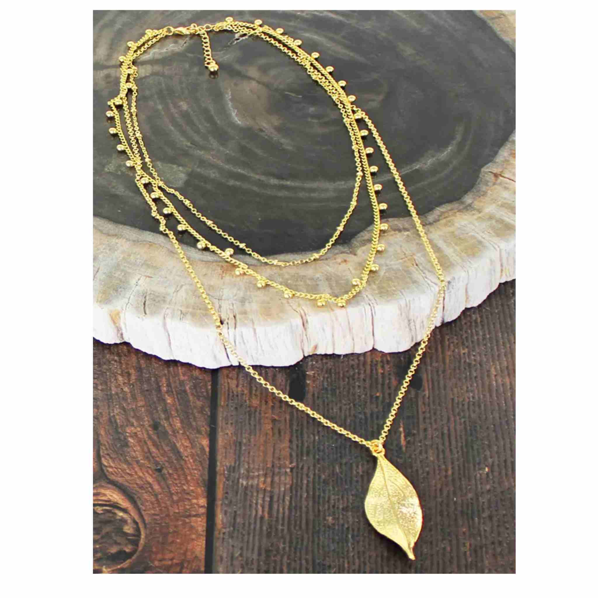 Gold necklaces with leaf pendant on a wooden surface