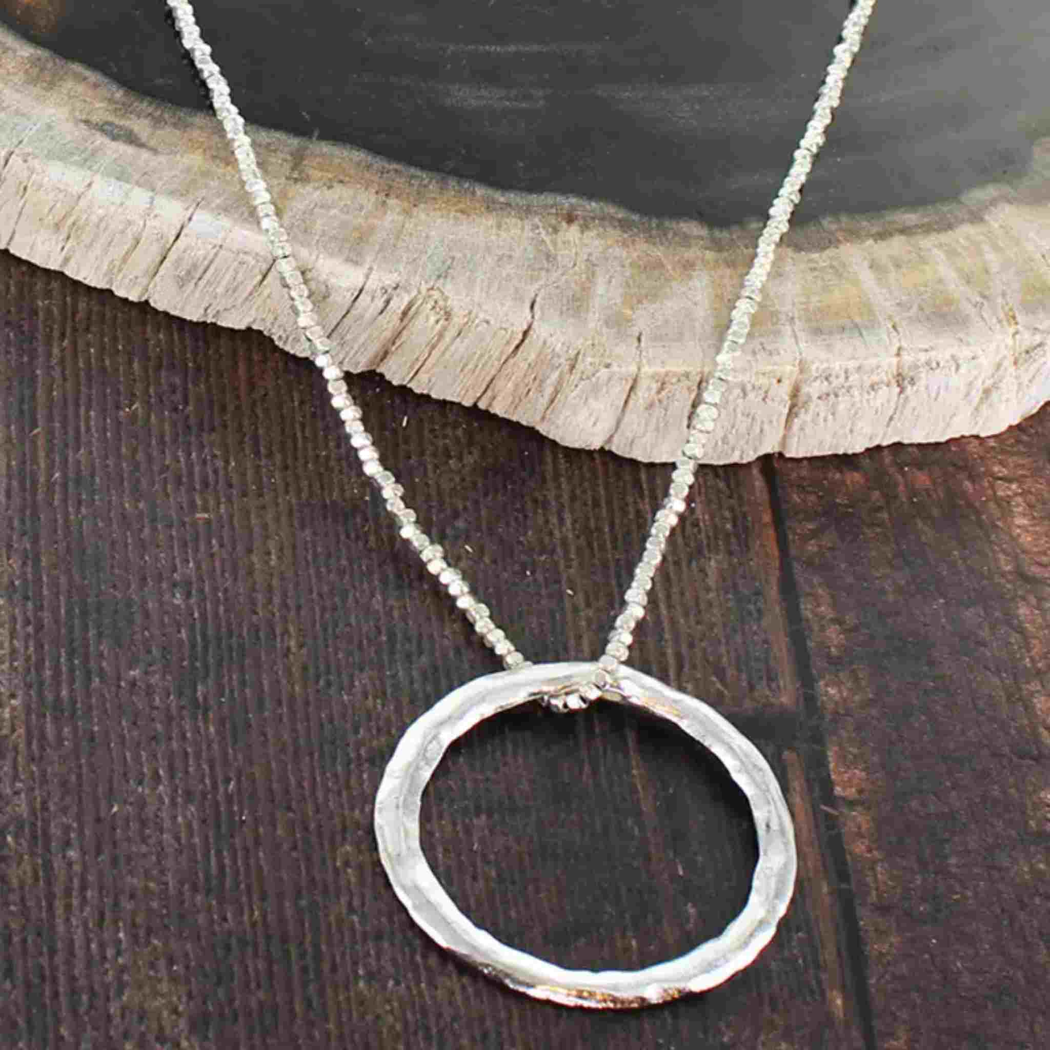 Silver necklace with a circular pendant on a wooden surface