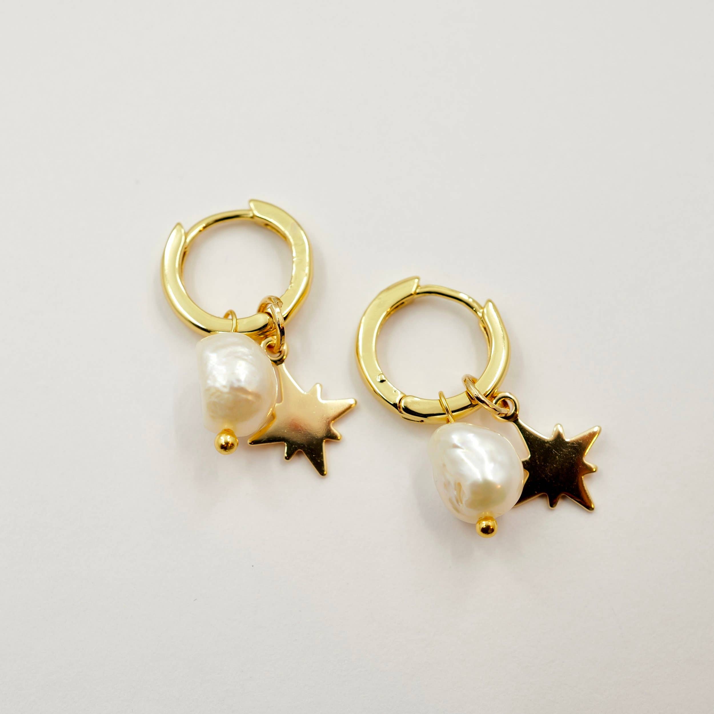 Gold hoop earrings with star and pearl charms on a light gray background