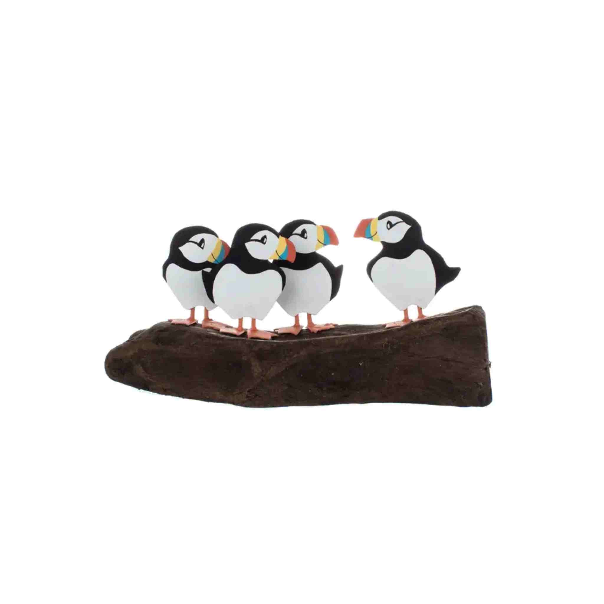 A decorative figurine of four puffin birds standing on a dark brown log, isolated on a white background.
