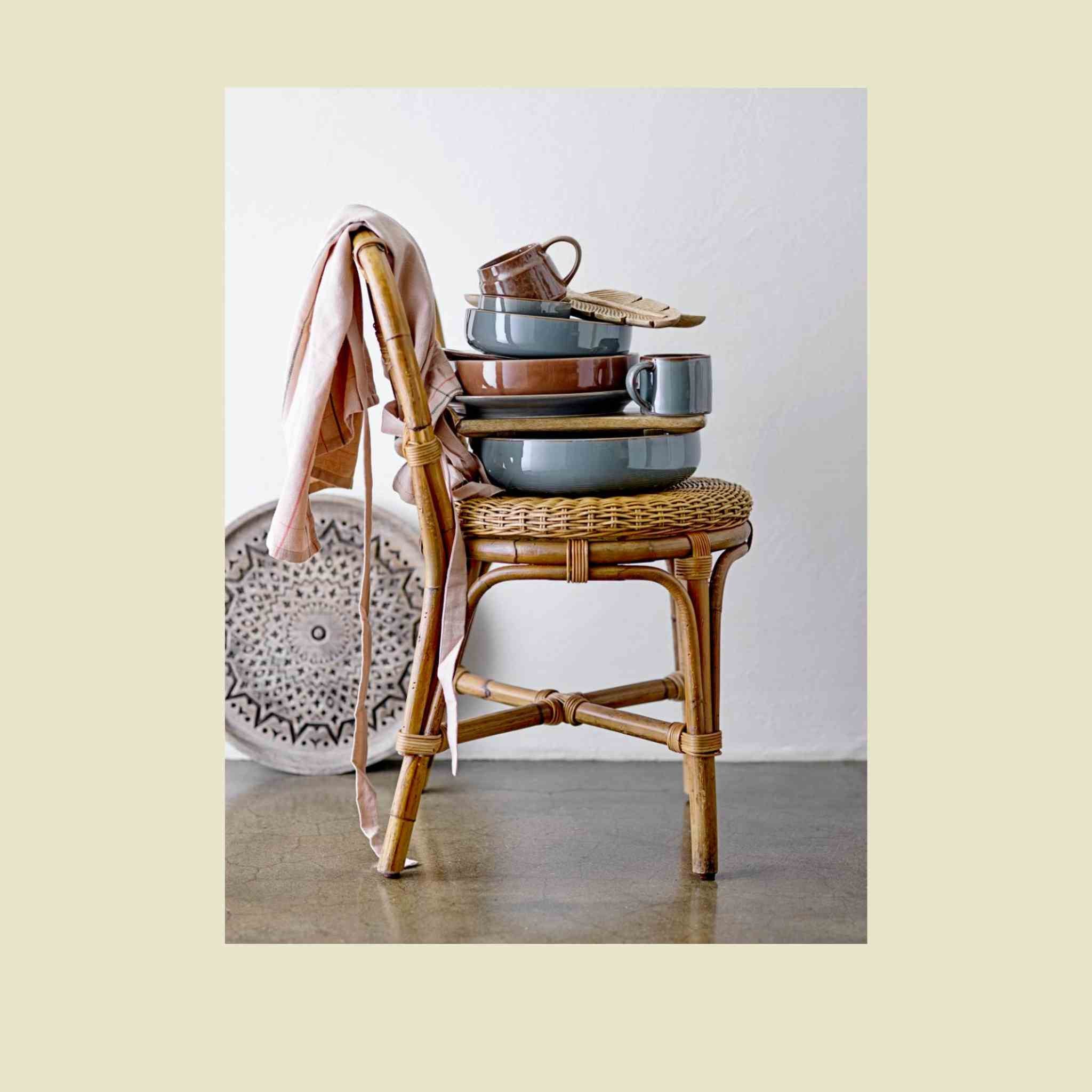Stack of ceramic dishes on a wicker chair with a white background