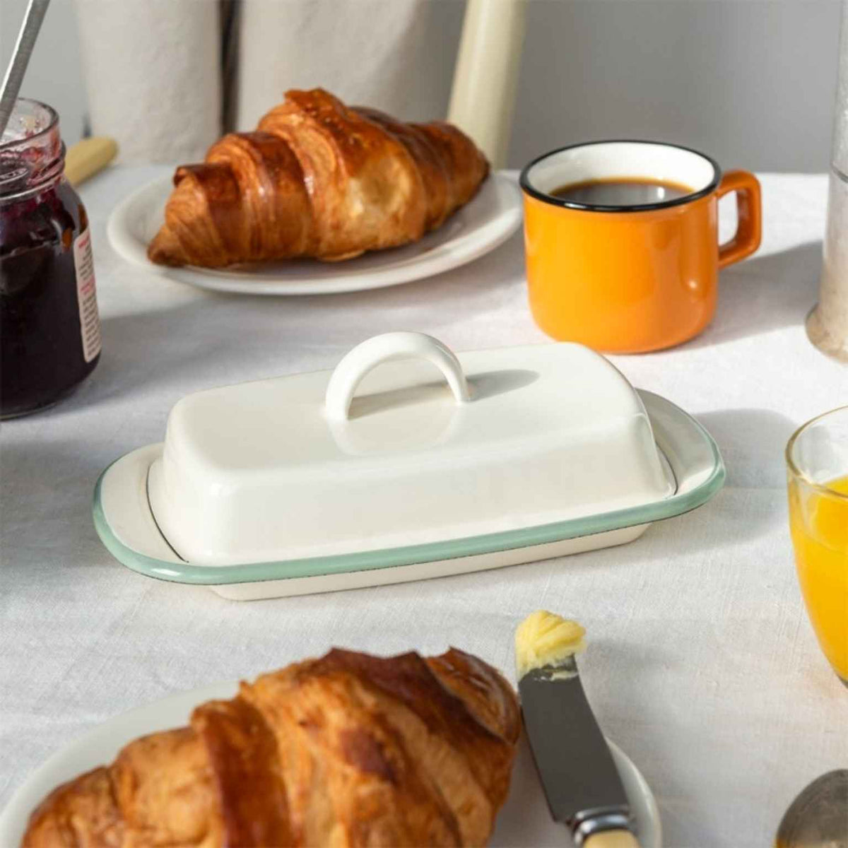 Butter dish on a table with croissants, coffee, and jam.