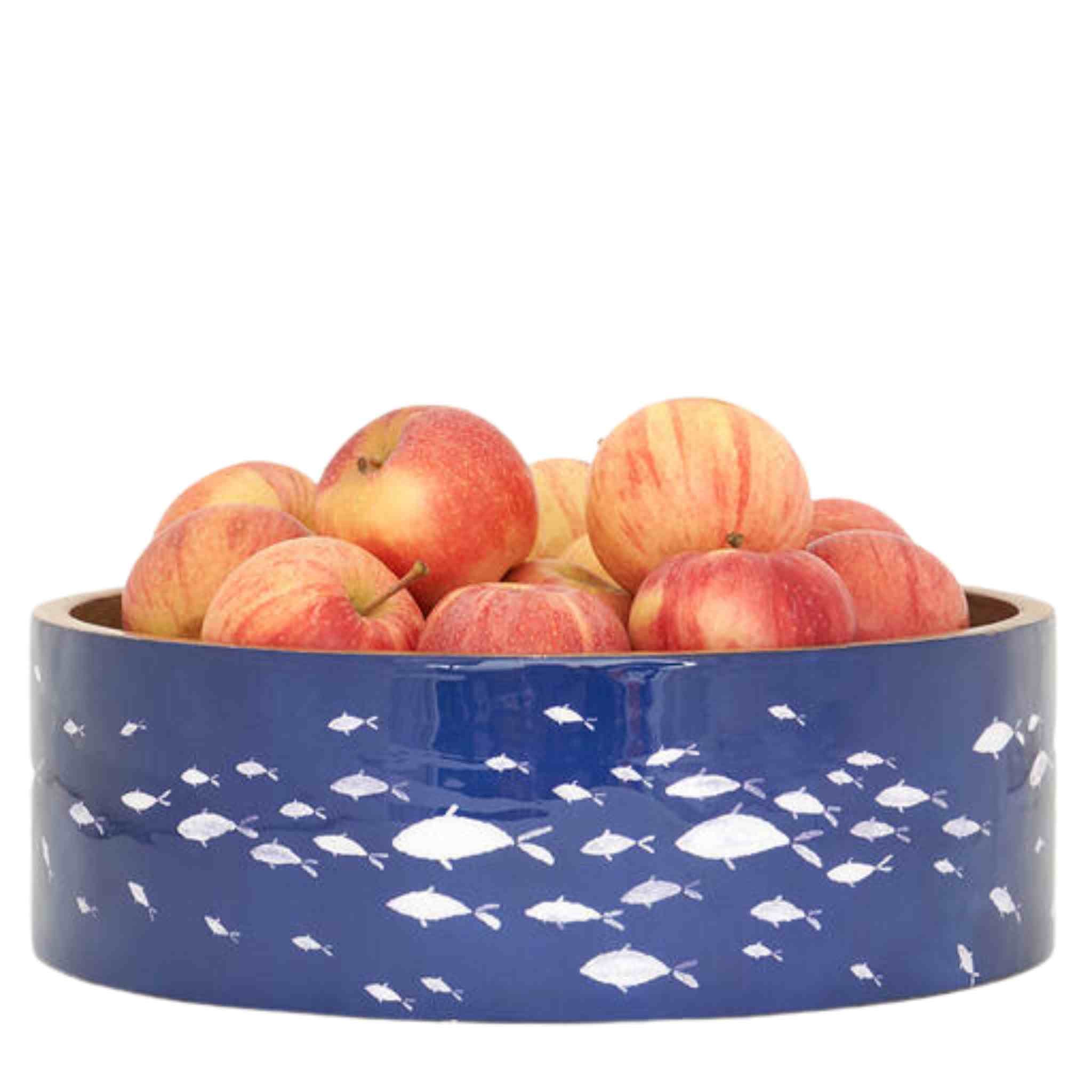 Blue bowl with white fish pattern filled with apples on a white background