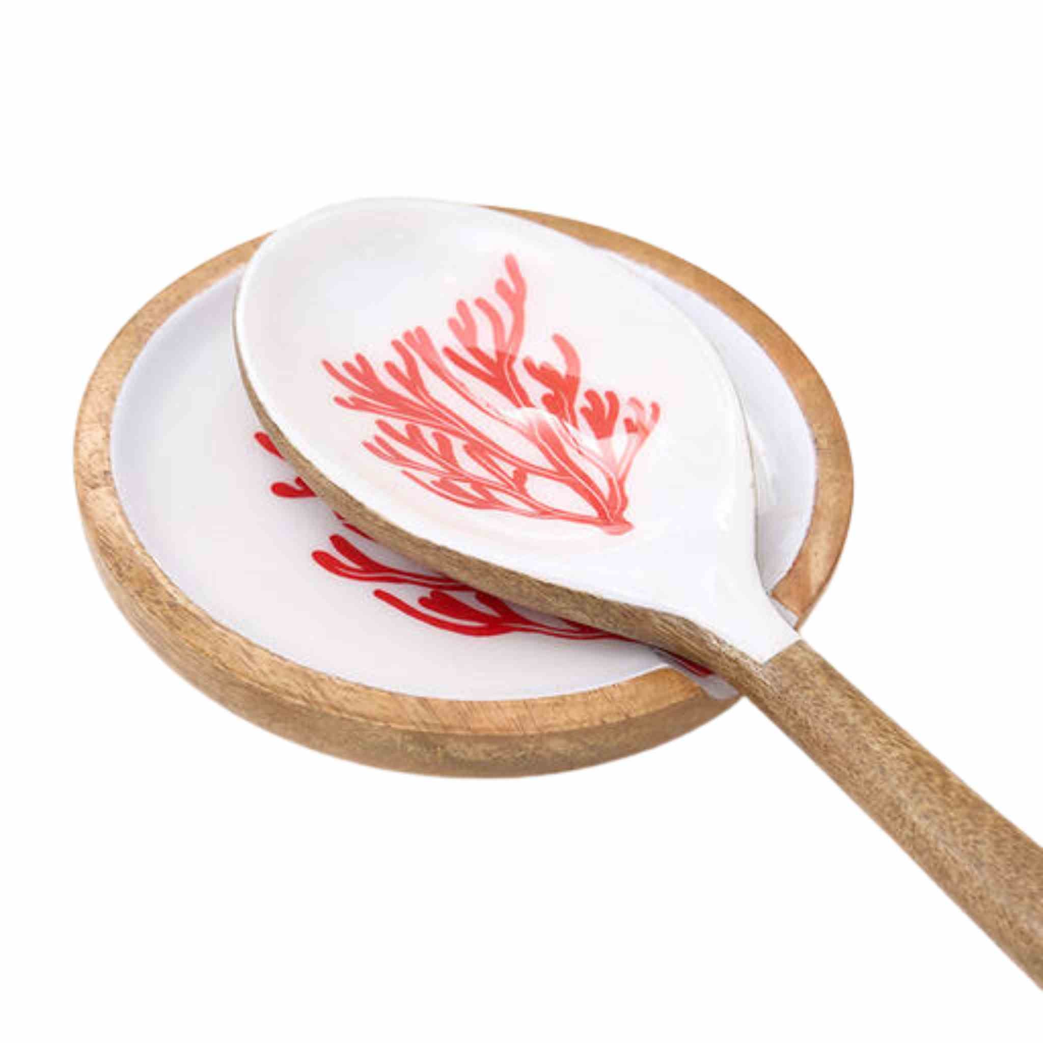 A white ceramic spoon with a red coral-like pattern, resting on a round wooden spoon rest against a white background.