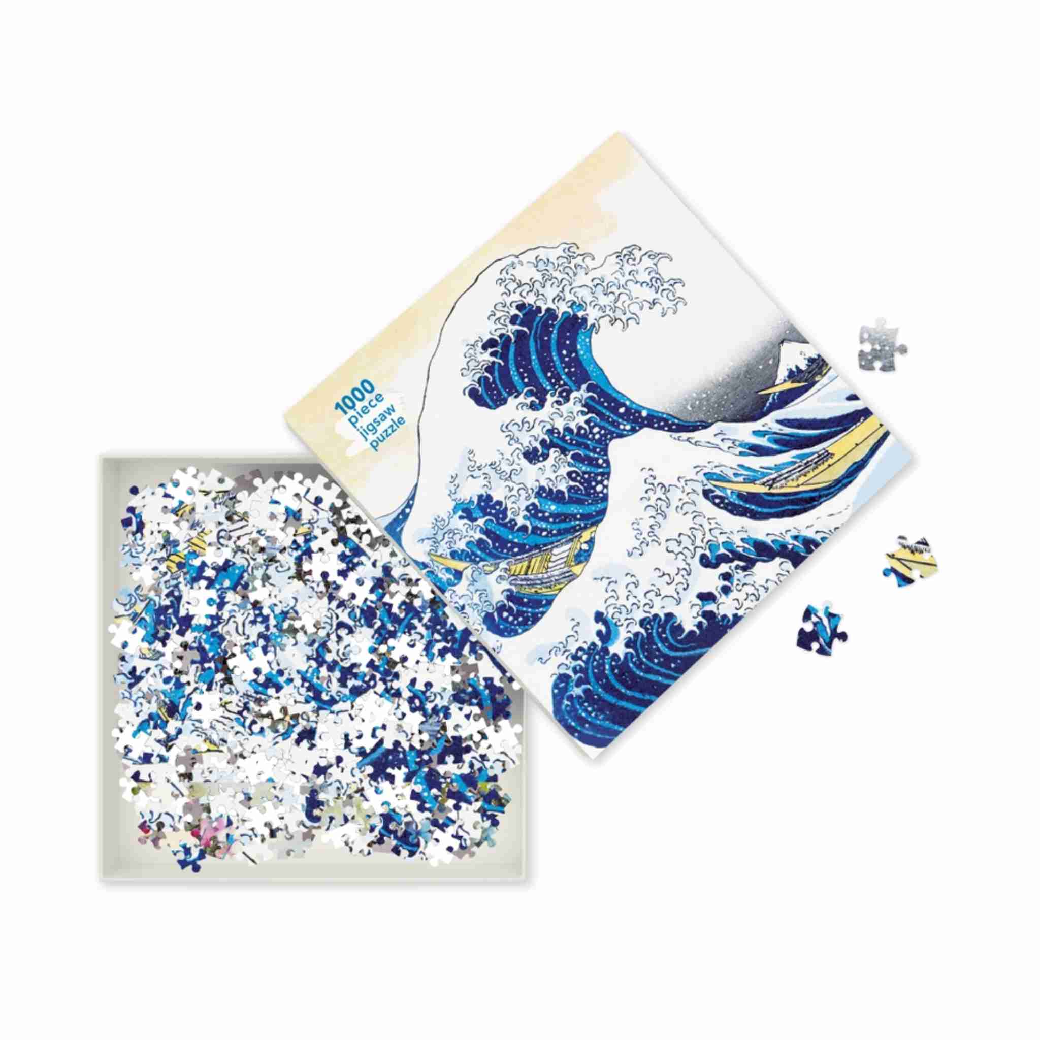 A 1000-piece jigsaw puzzle featuring Hokusai's Great Wave off Kanagawa, shown with its box, a tray of loose pieces, and a few scattered pieces on a clean white background.