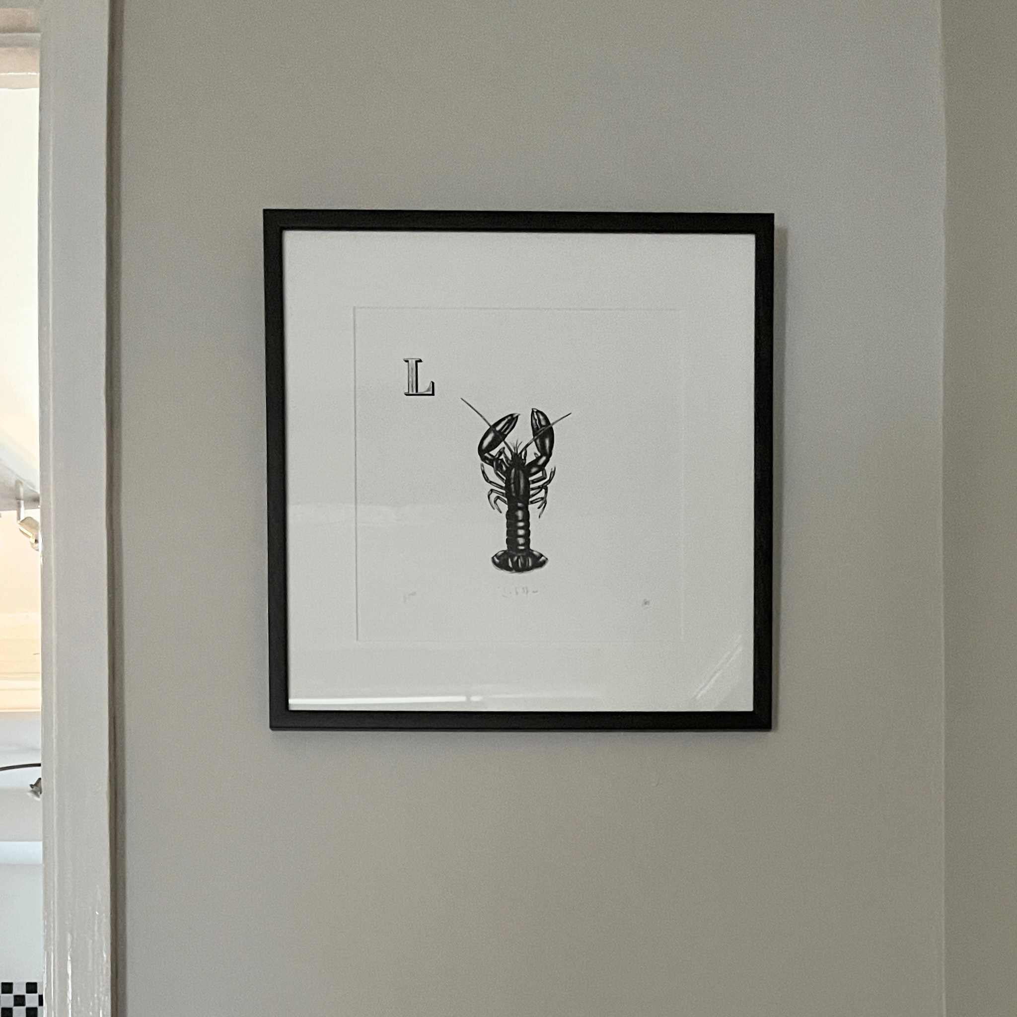 Framed artwork of a black and white lobster on a light gray wall.