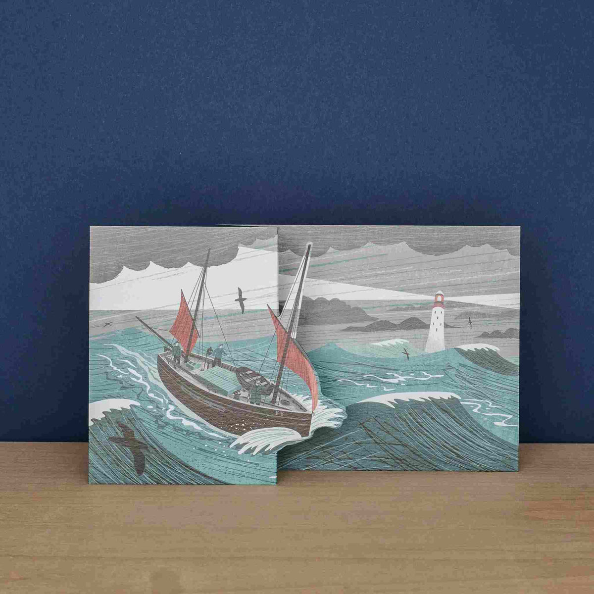 Card with a sailboat and lighthouse design on a wooden surface and blue background