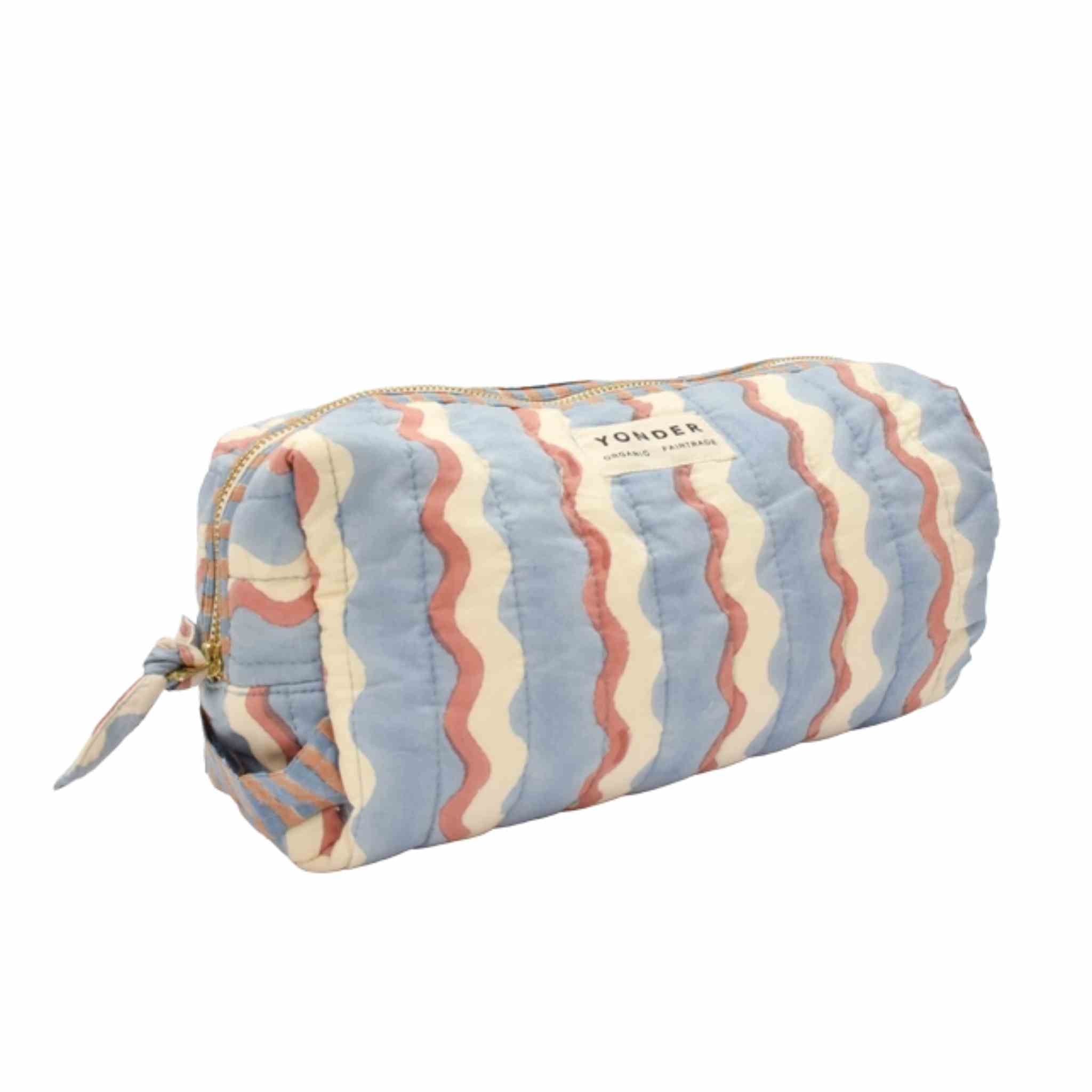 A quilted cylindrical cosmetic pouch with a wavy stripe pattern in light blue, cream, and terracotta, featuring a gold zipper and a YONDEL brand label.