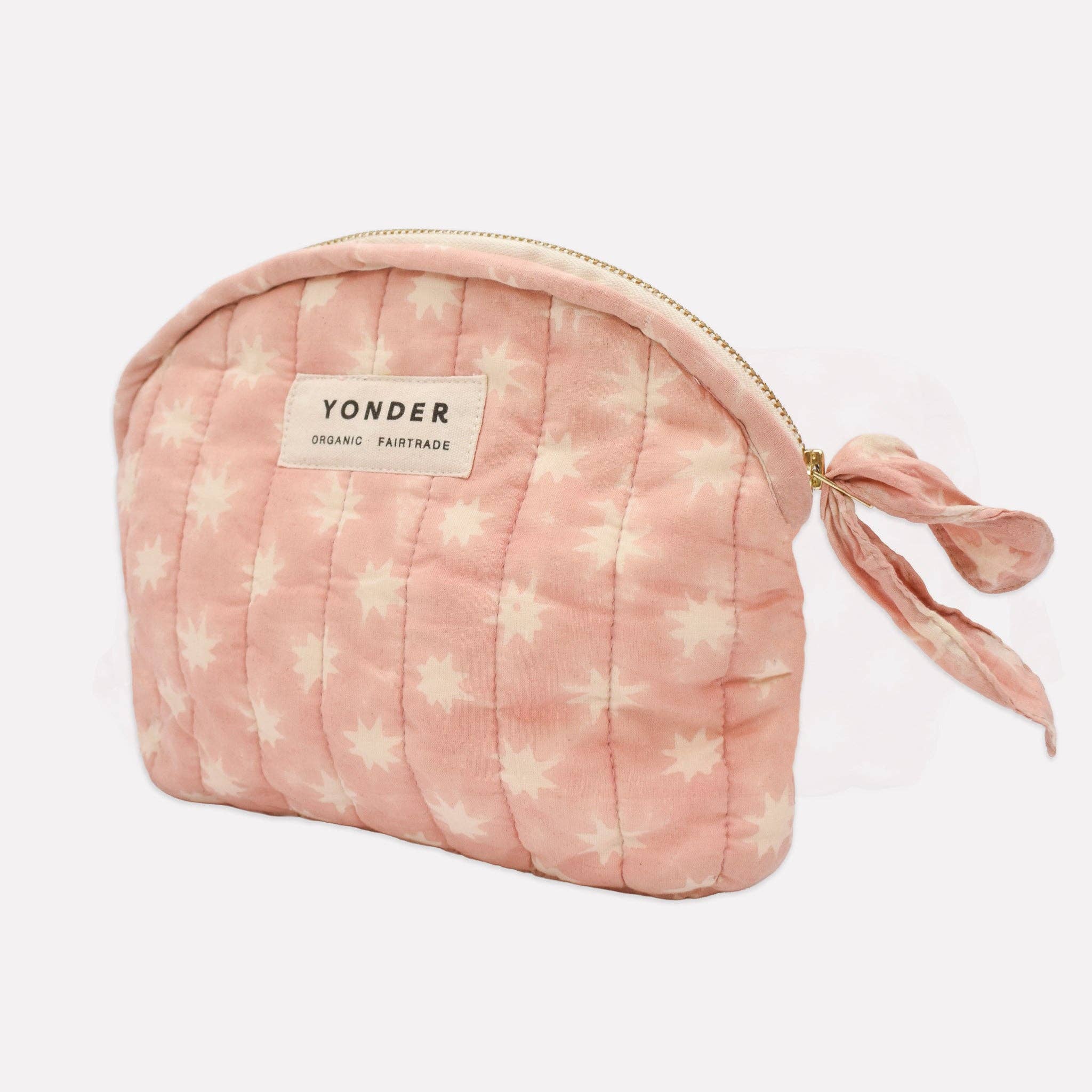A pink quilted cosmetic pouch with a white star pattern, featuring a cream-colored YONDER brand label and a matching pink fabric tie at the zipper.