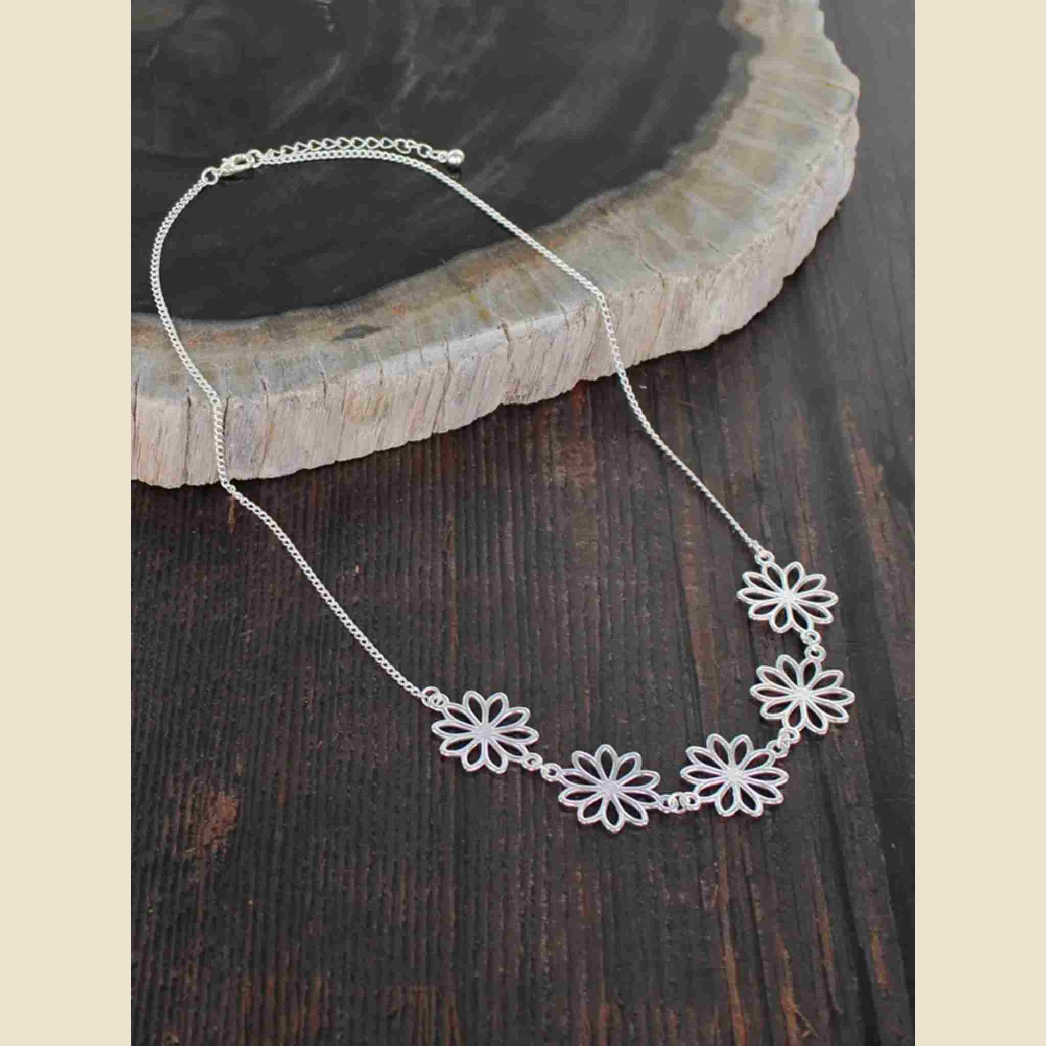 Silver necklace with floral designs on a wooden surface