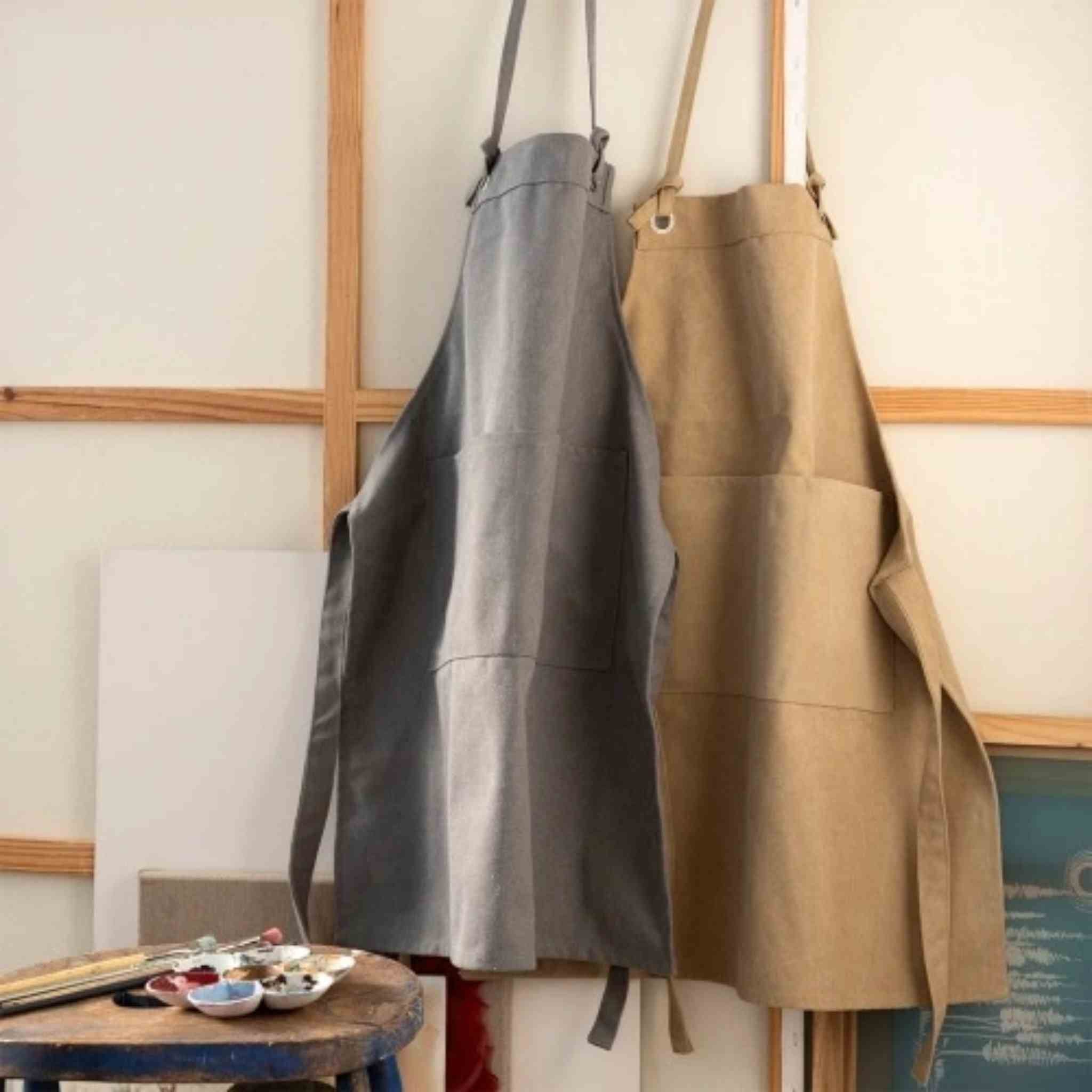 Two aprons, one gray and one brown, hanging on a rack against a wall.