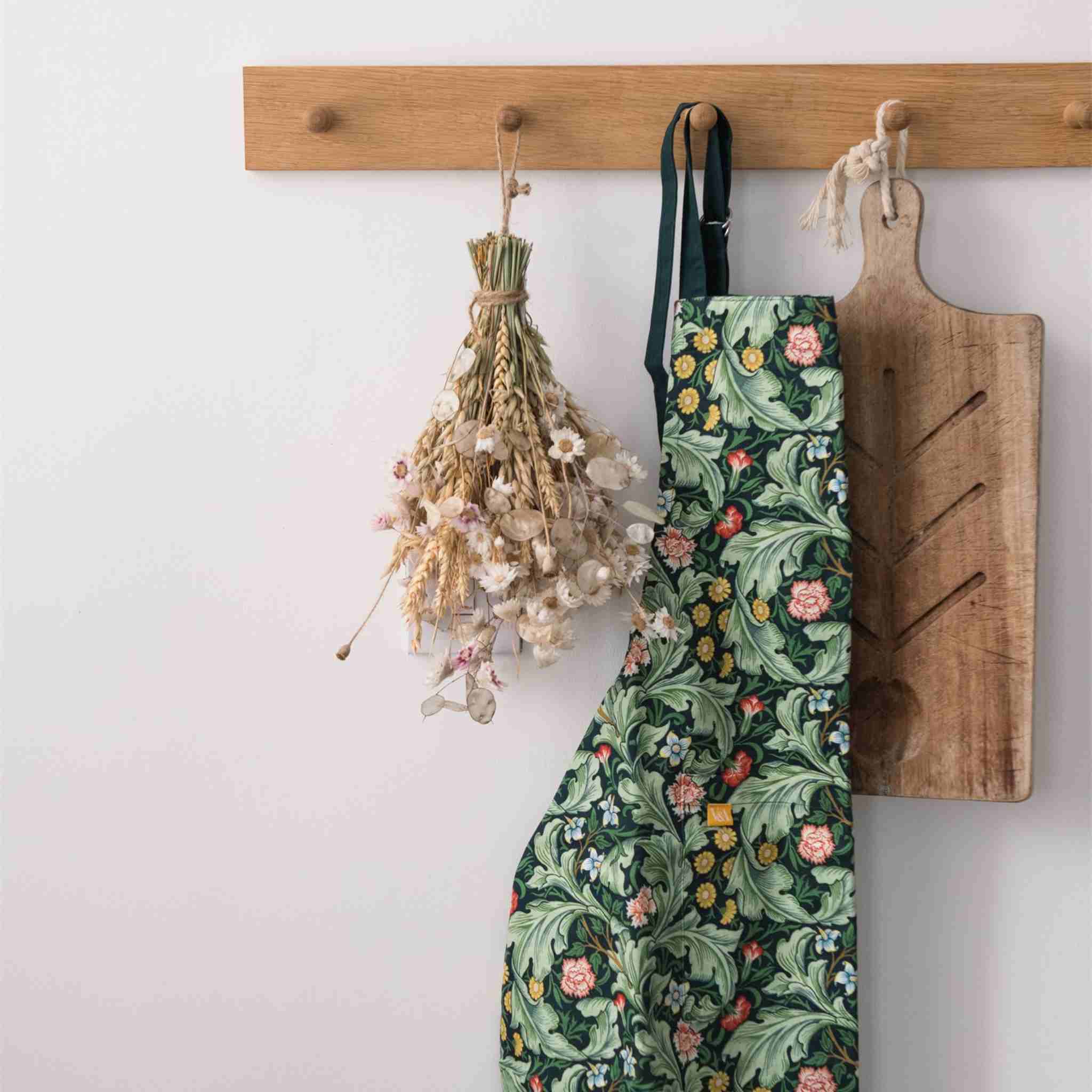 Floral apron hanging on a wooden rack with a cutting board and dried flowers.