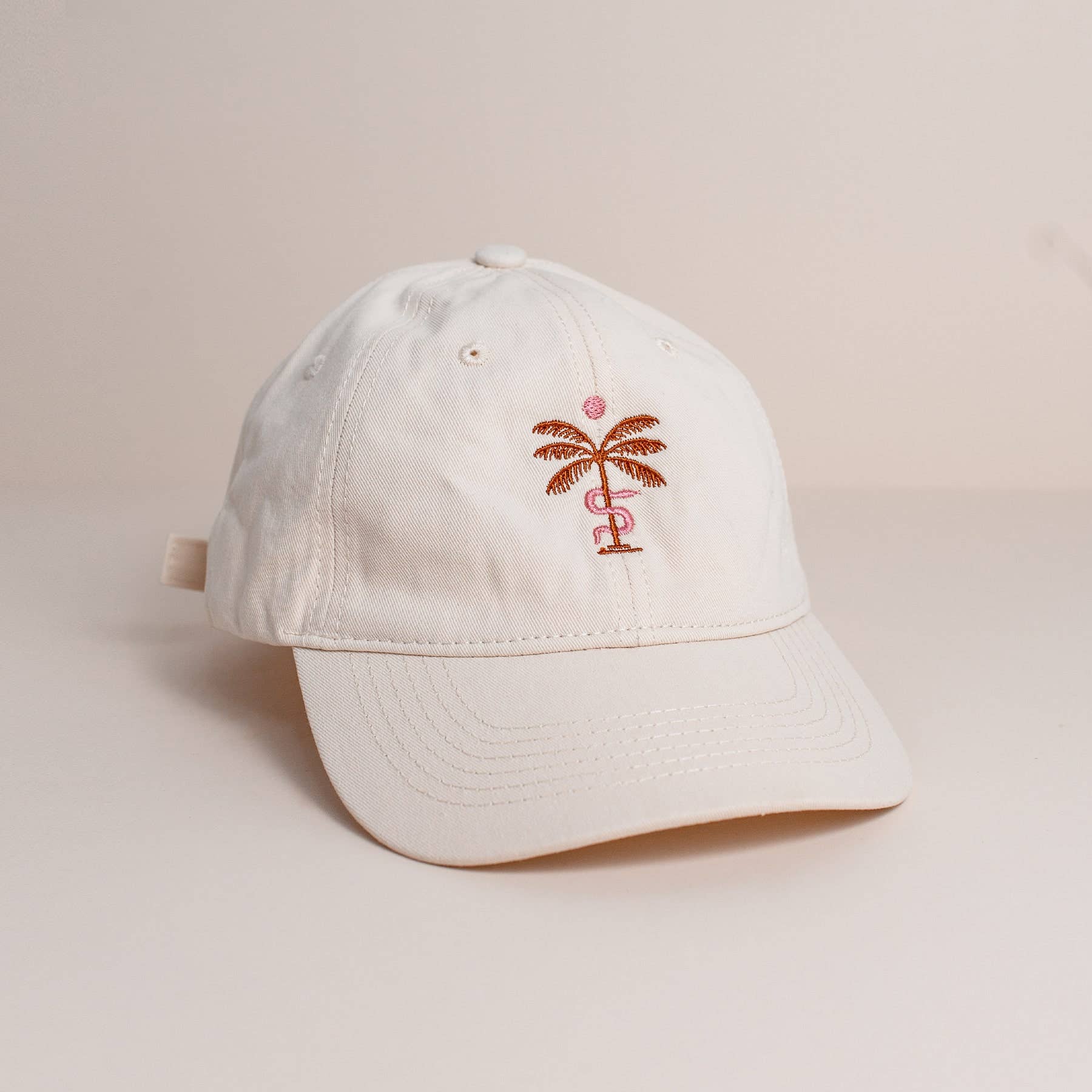 White cap with a palm tree design on a beige background