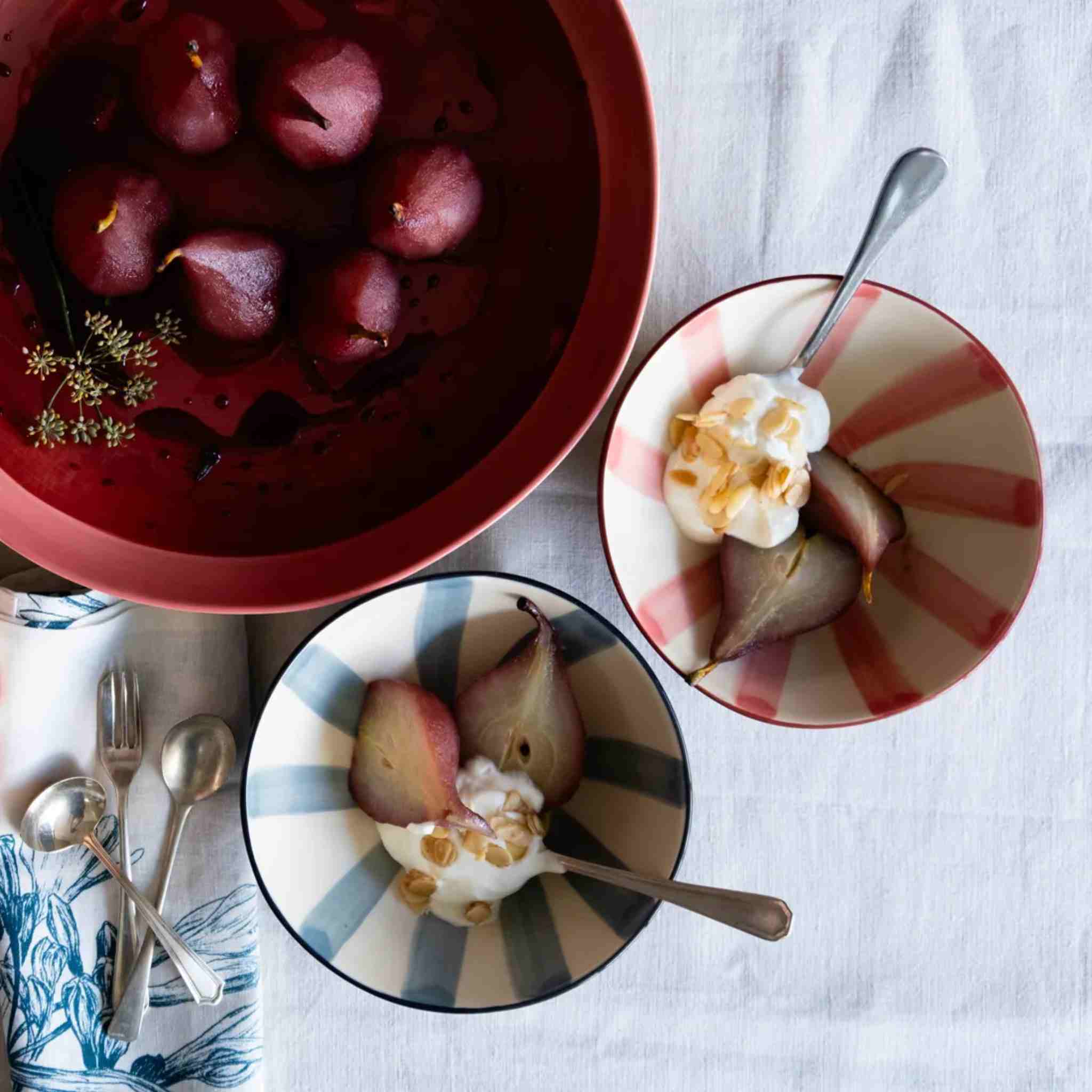 Bowls of poached pears with yogurt on a table setting.