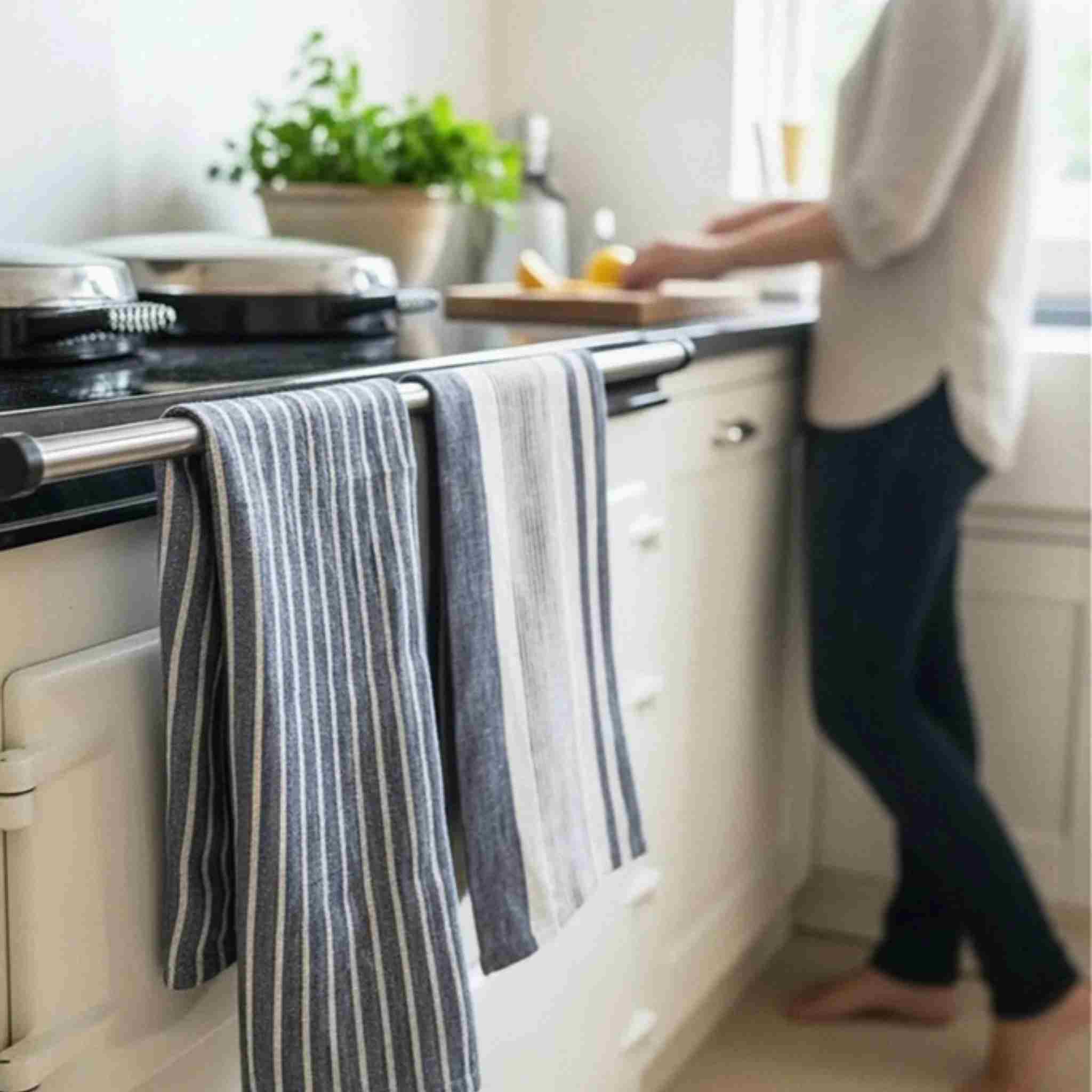 Two navy kitchen towels hanging from a silver metal handle on a white oven in a bright kitchen.