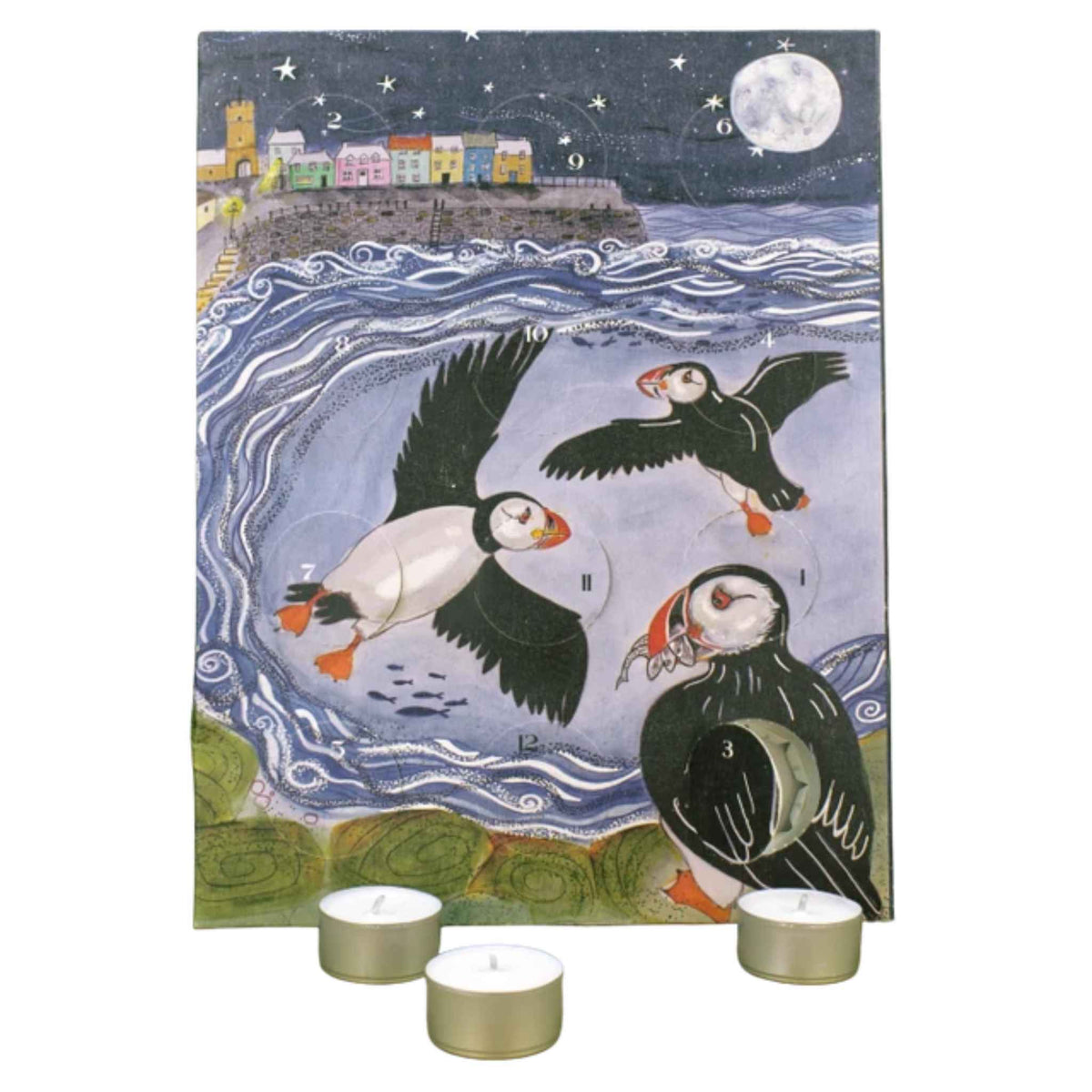 An illustrated advent calendar featuring puffins in a stylized coastal scene with a moon, stars, and colorful buildings. Three small tealight candles sit in front on a white background.