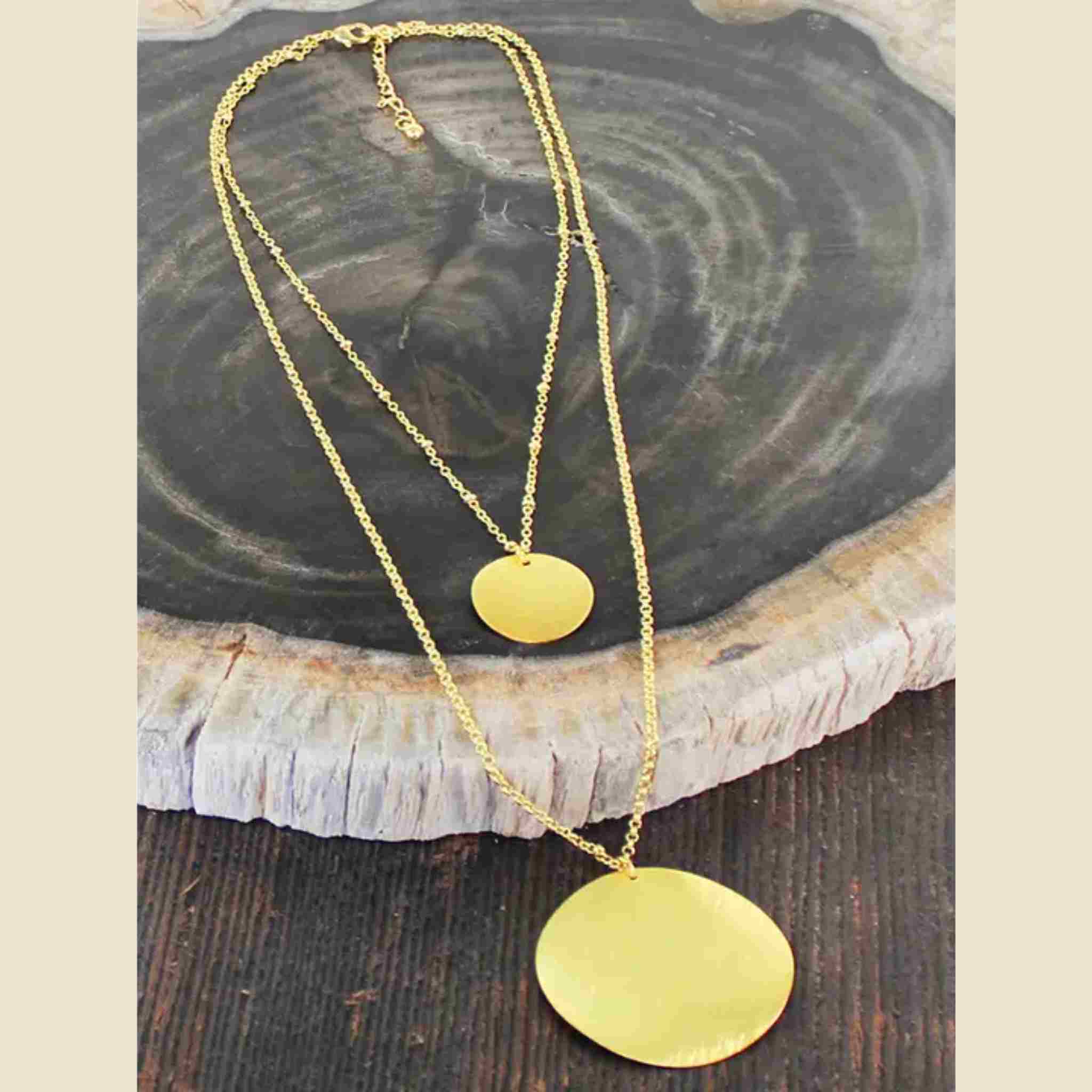 Gold necklace with two round pendants on a wooden surface