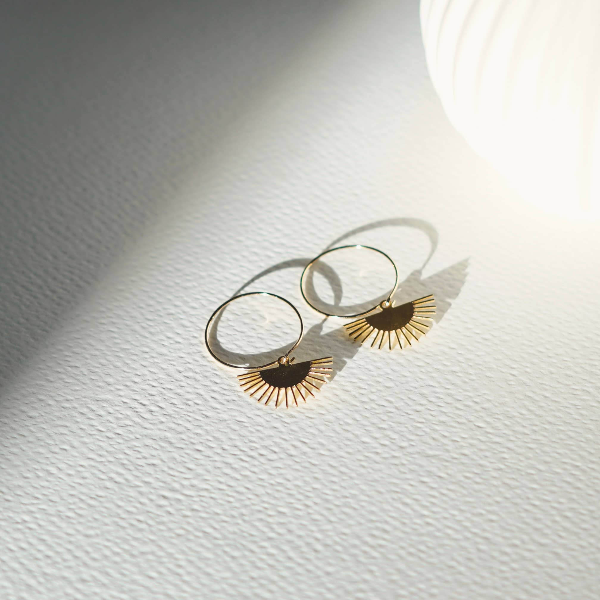 Gold earrings with sunburst designs on a textured white surface