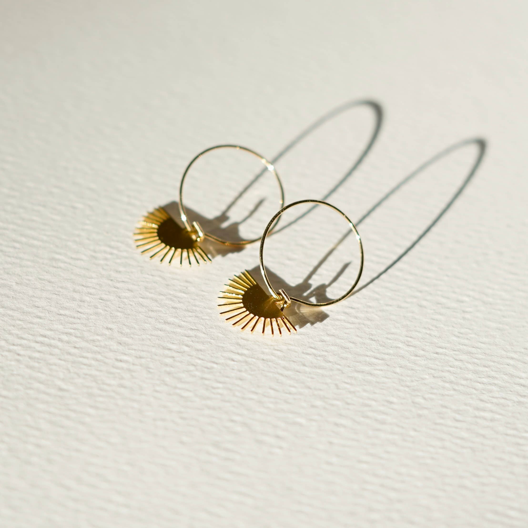 Gold hoop earrings with sunburst designs on a light background