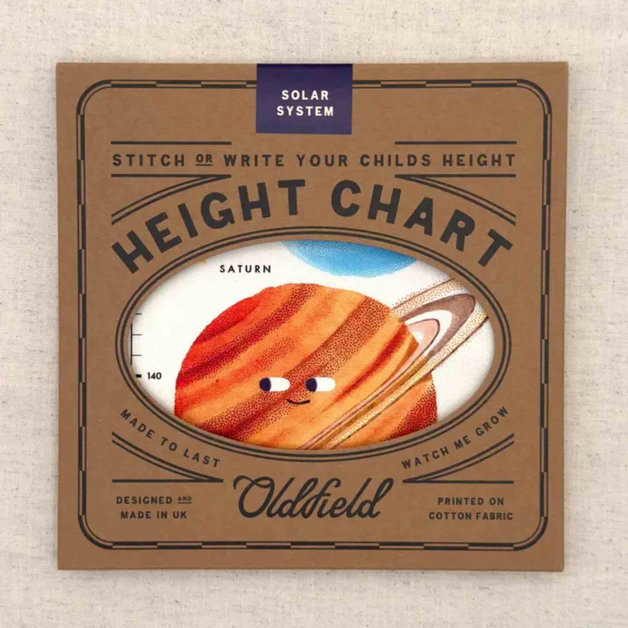 A square brown fabric height chart for children by Oldfield, featuring a cartoon illustration of Saturn in the center. The top has a blue 'Solar System' label, and the fabric is displayed flat on a light textured background.