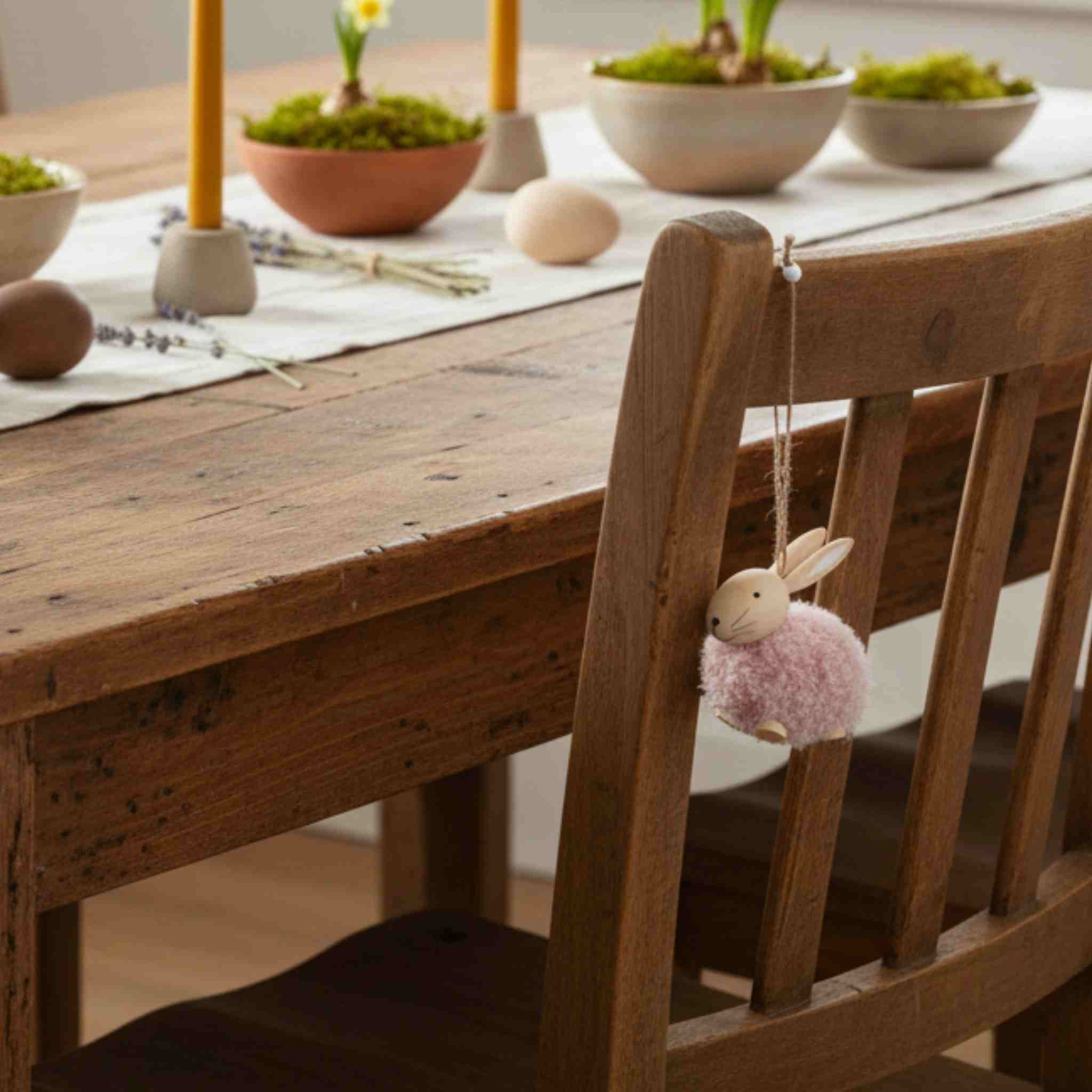 Wooden chair with a decorative rabbit ornament hanging on it, set against a dining table with Easter decorations.