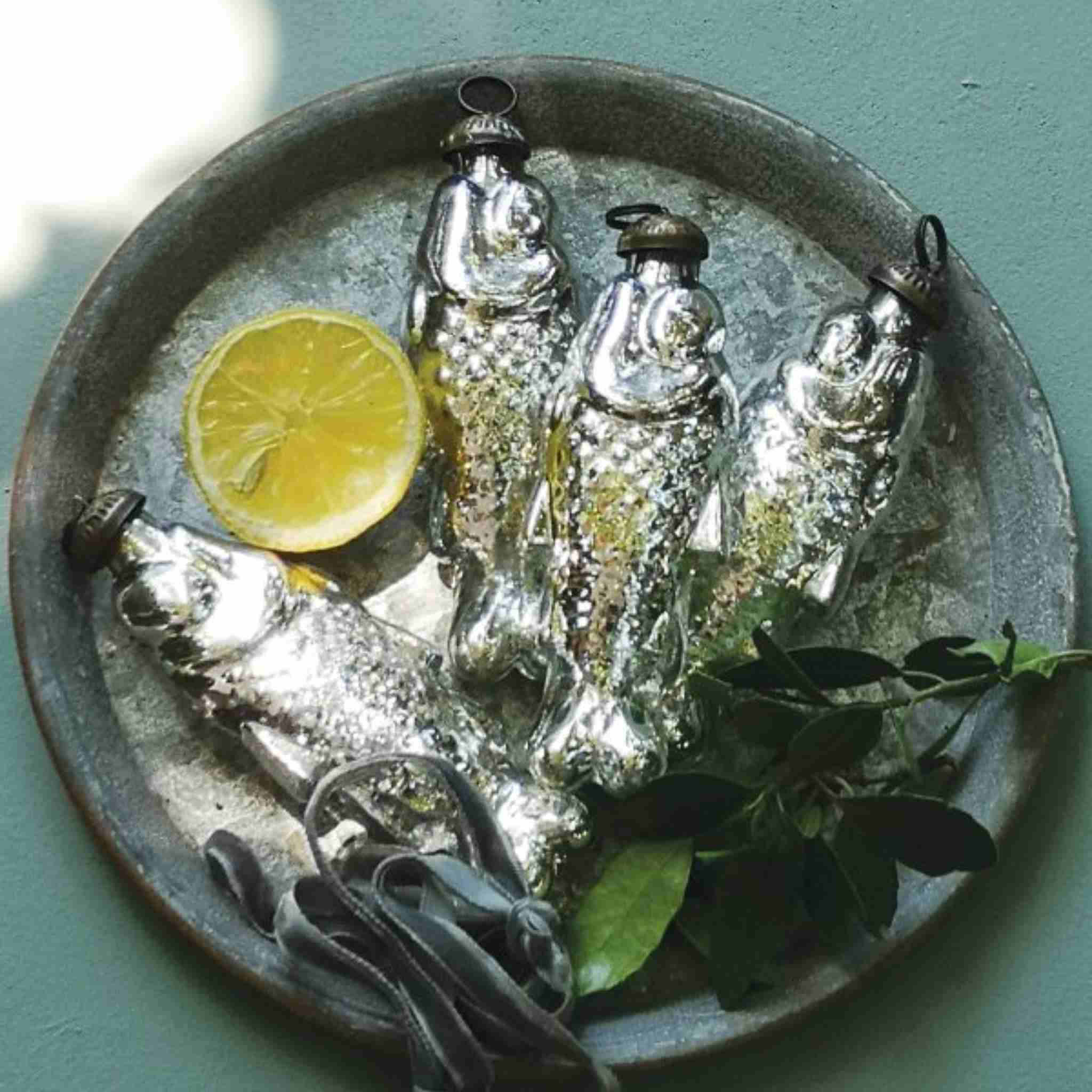 Silver fish decorations on a metal plate with a lemon wedge and green leaves