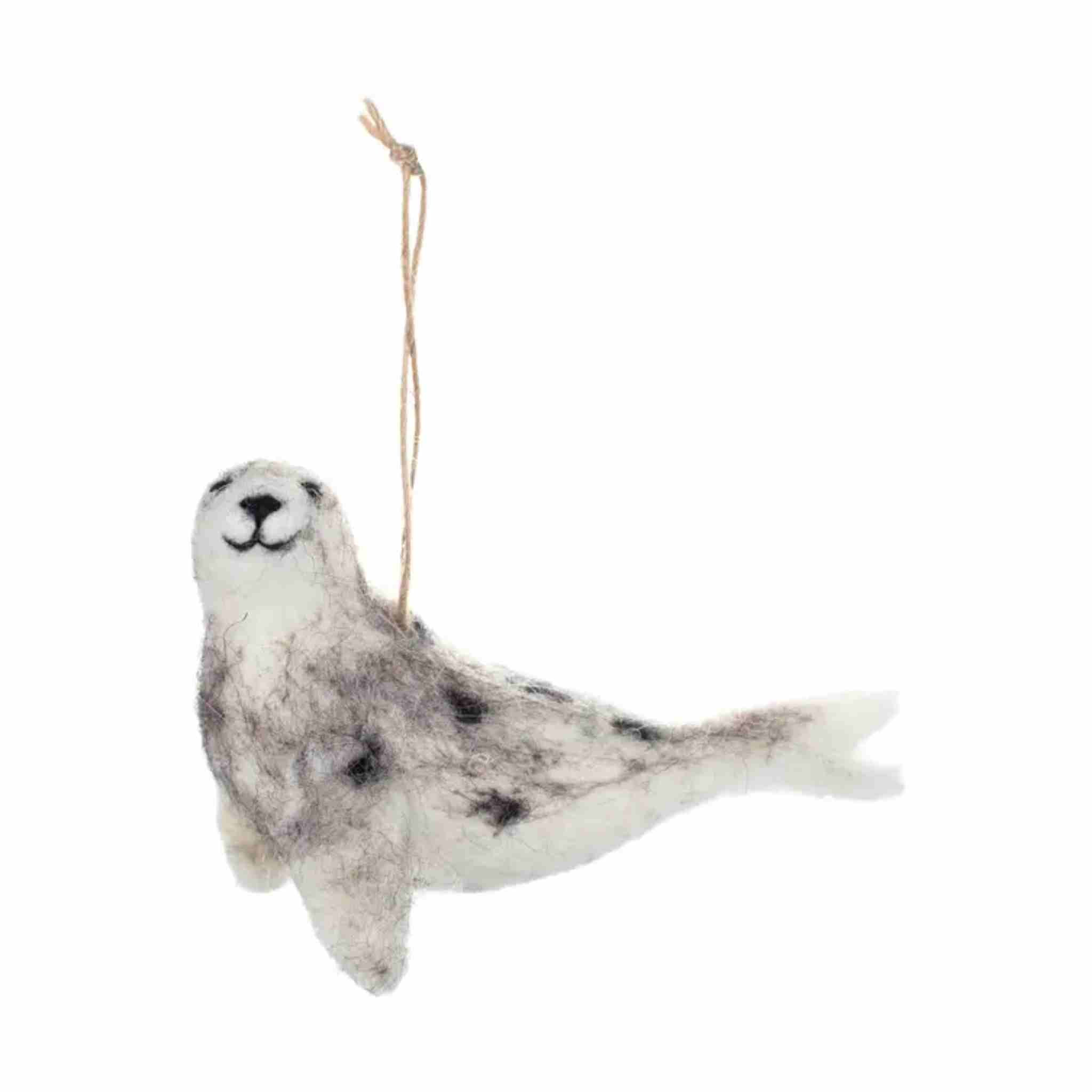 A felted wool seal ornament in white and gray with black spots, hanging from a thin natural twine string against a plain white background.