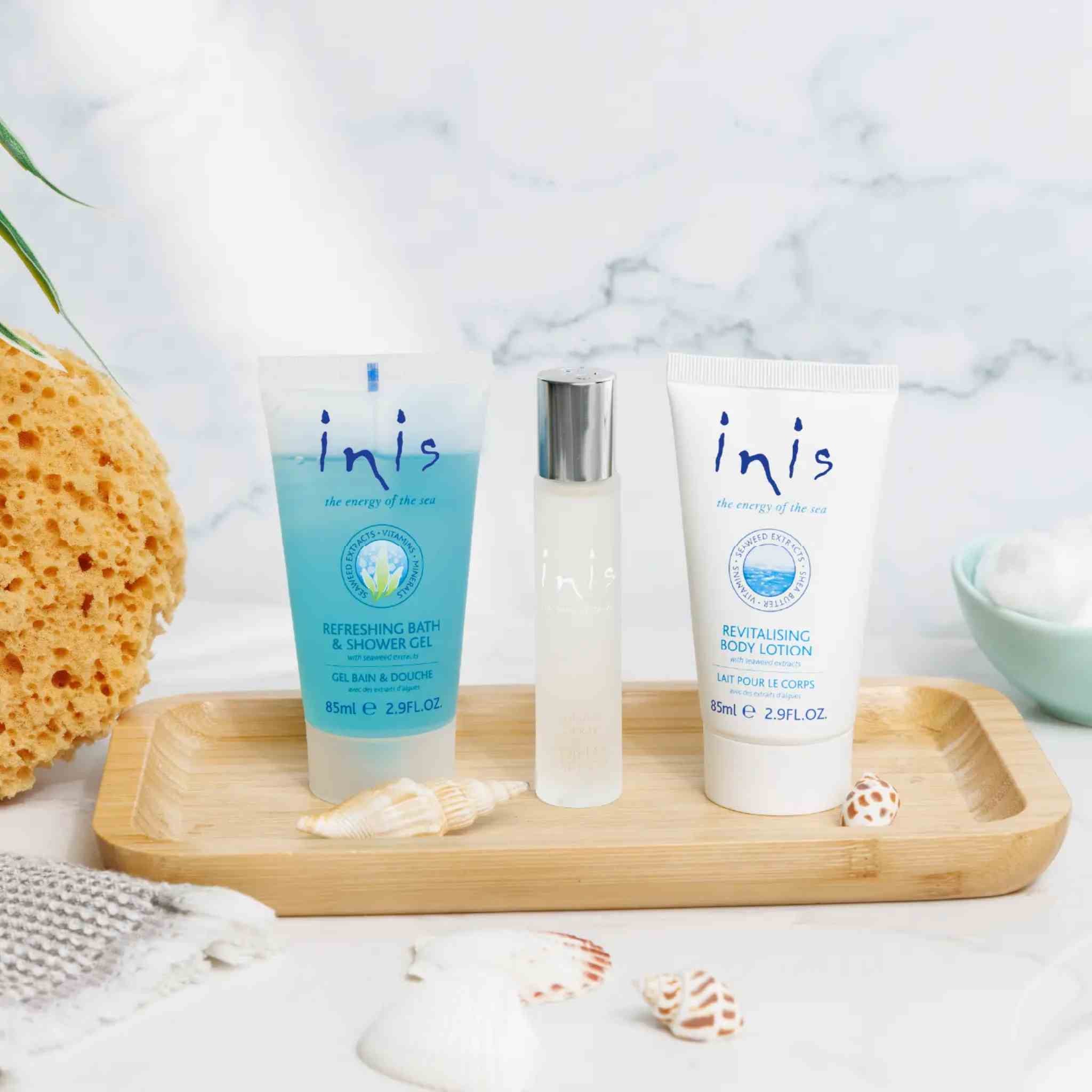 Three Inis body care products arranged on a light wood tray