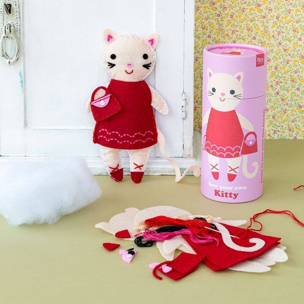 Cat-shaped doll with a red dress and accessories next to a cylindrical packaging labeled 'Kitty'.