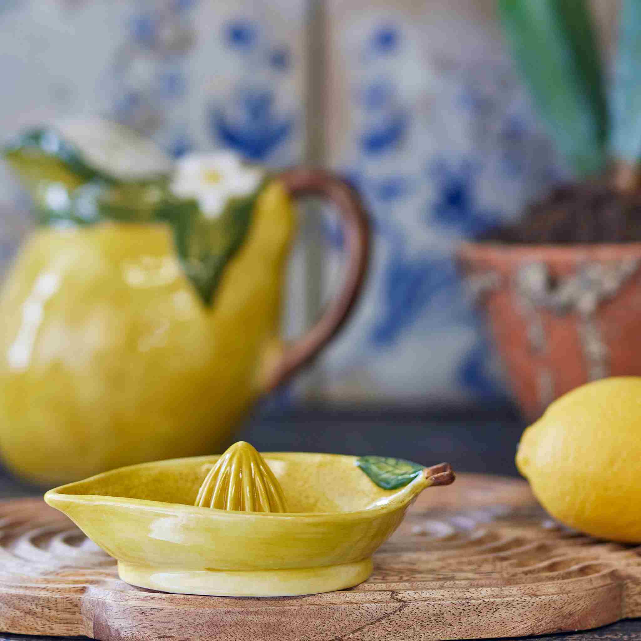 Yellow ceramic lemon squeezer on a wooden surface with a floral-patterned teapot in the background.