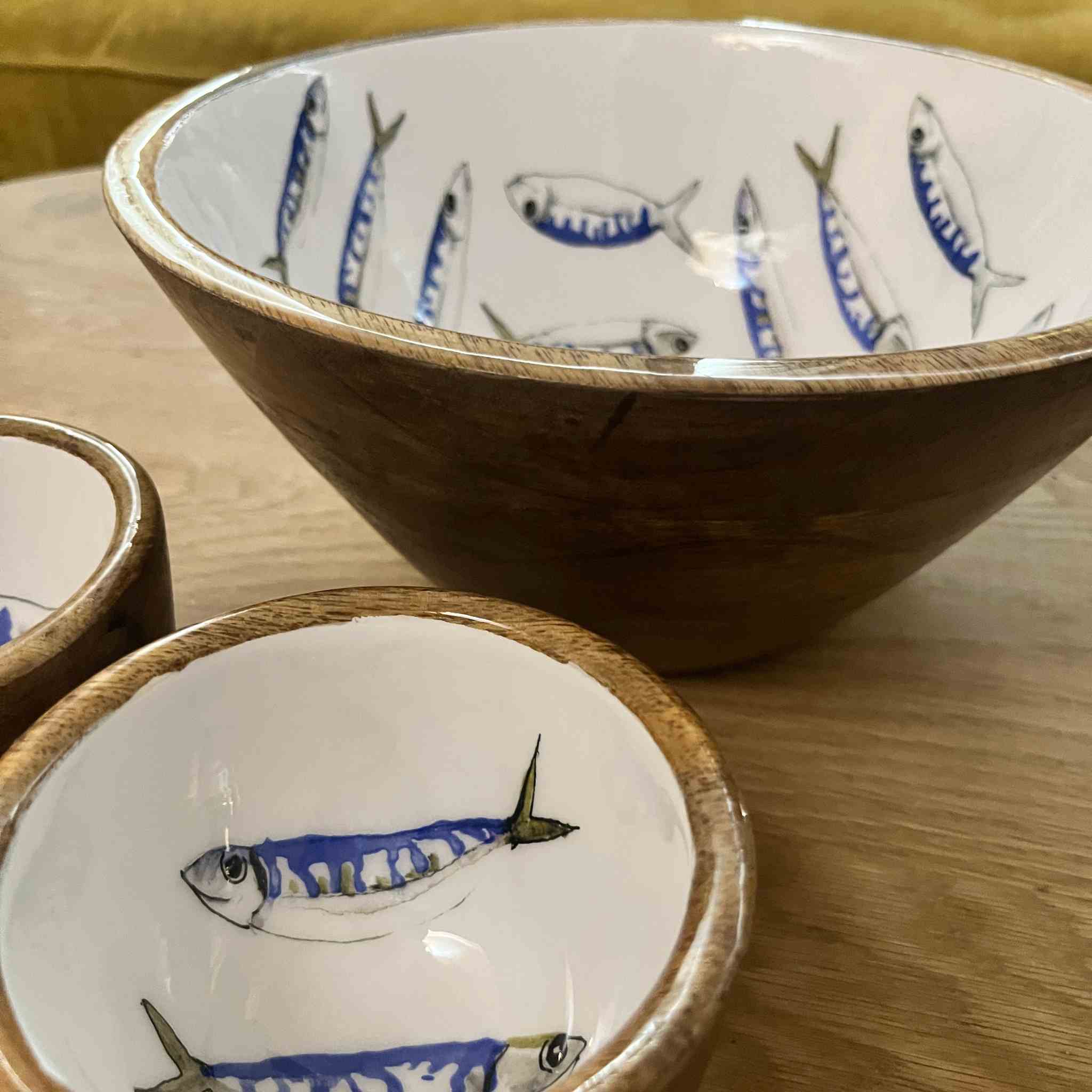 A set of hand-painted ceramic bowls with a natural wood rim and a white interior decorated with blue and black fish illustrations, shown on a wooden table.