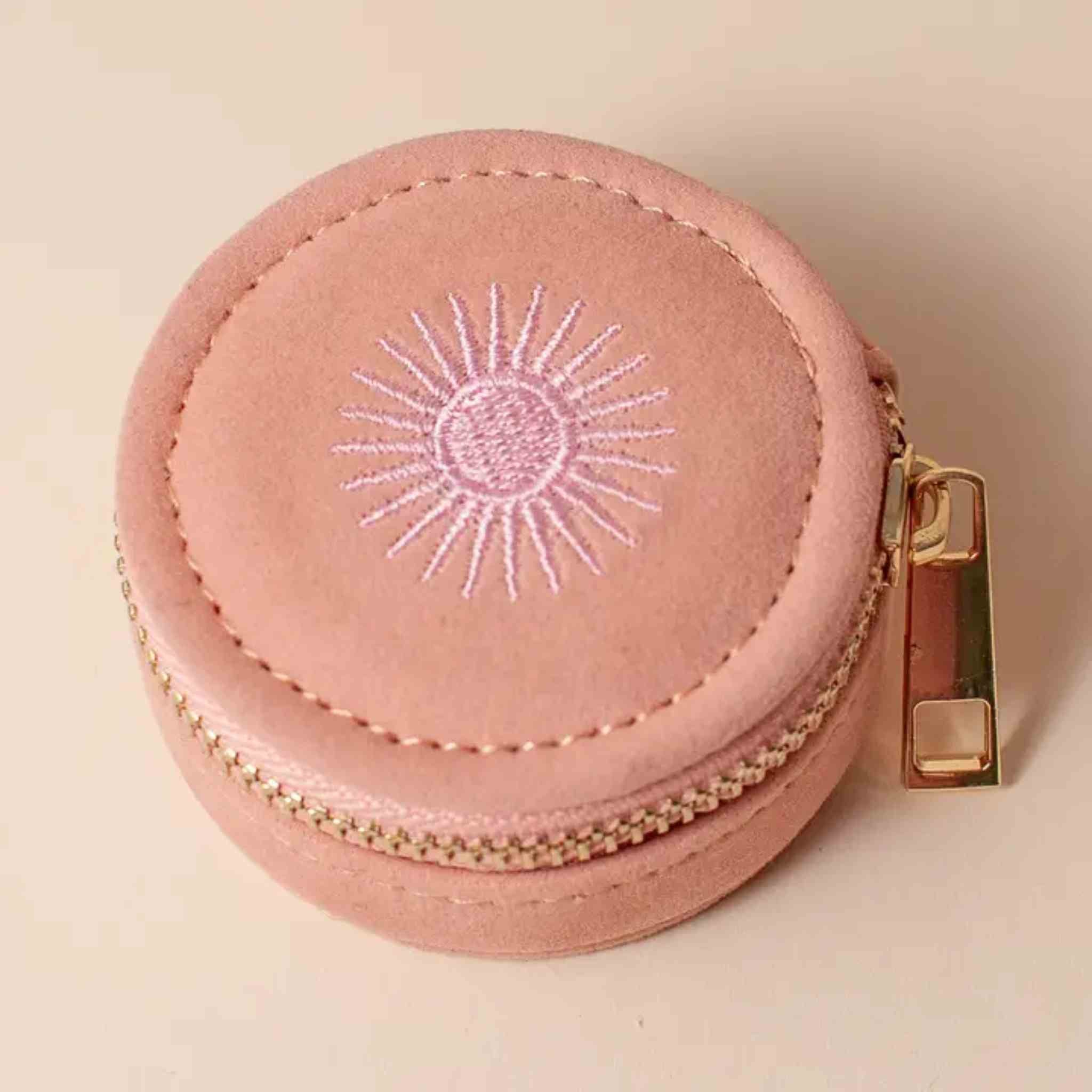 Pink round jewelry case with sun design and gold zipper on a beige background