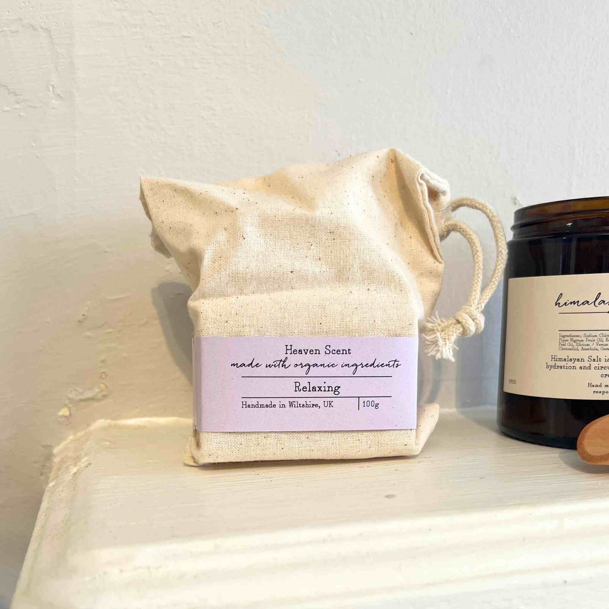 natural soap product in a drawstring bag on a white mantelpiece with a candle in the background.