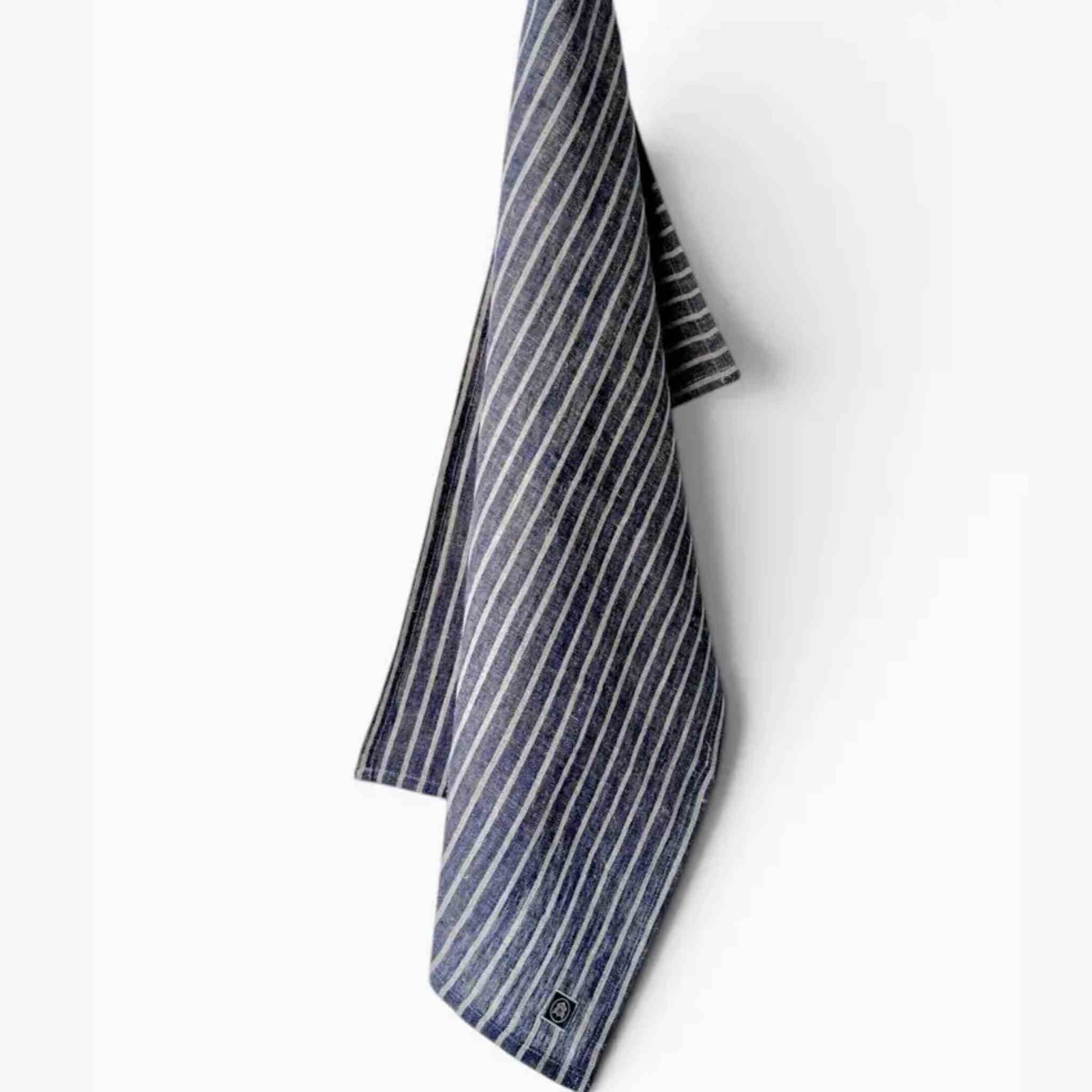 A folded striped tea towel  featuring vertical navy and white stripes, hanging against a plain white background.