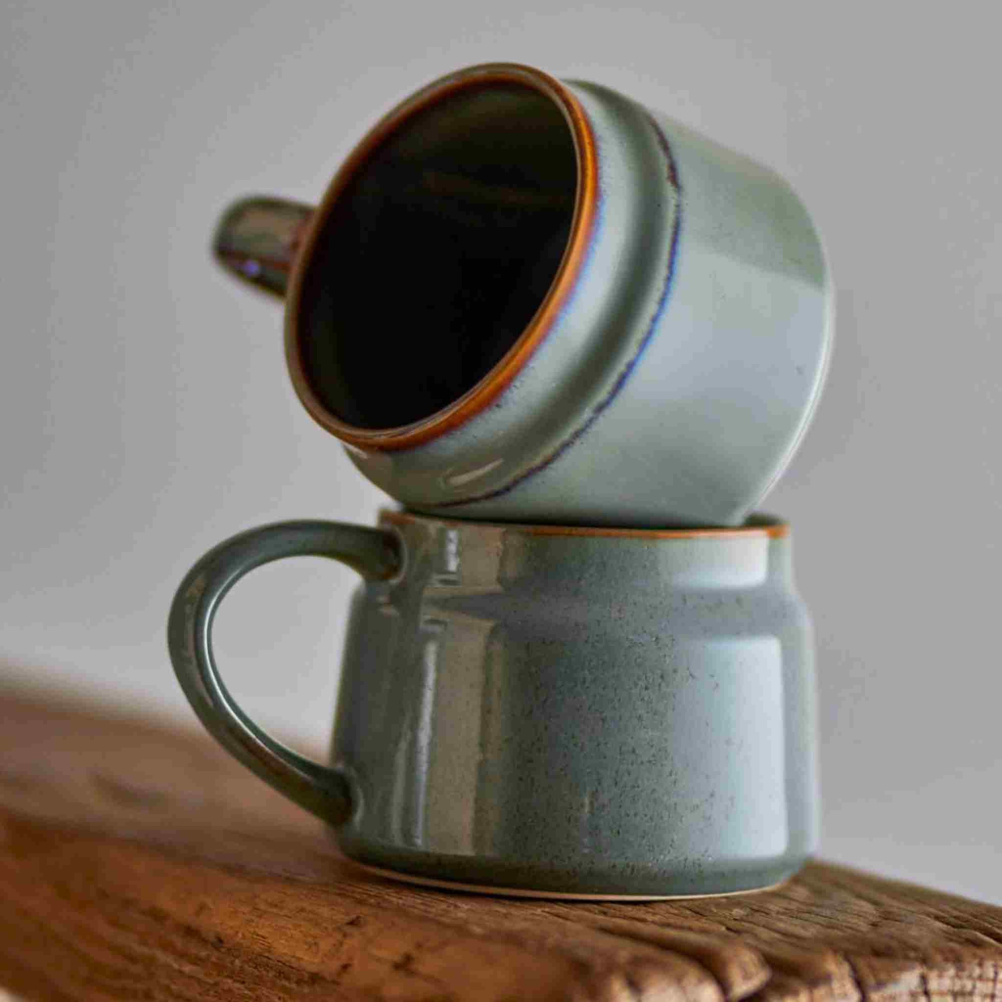 Two stacked ceramic mugs on a wooden surface with a neutral background
