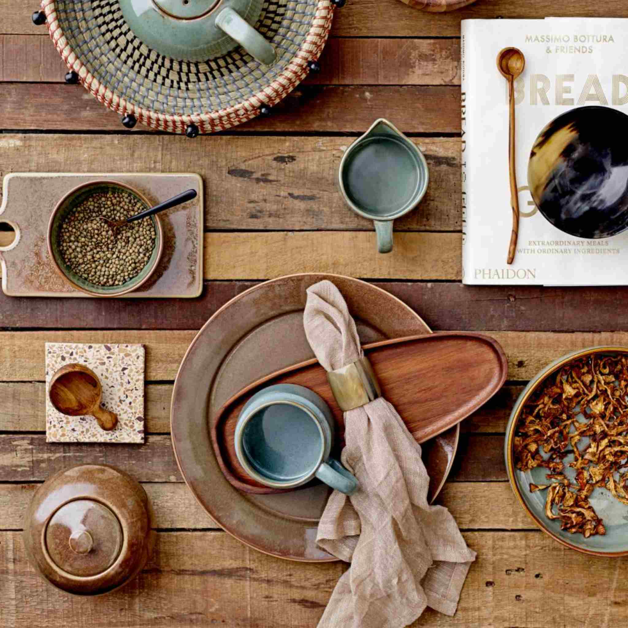 Table setting with ceramic dishes, mugs, and a book on a wooden surface