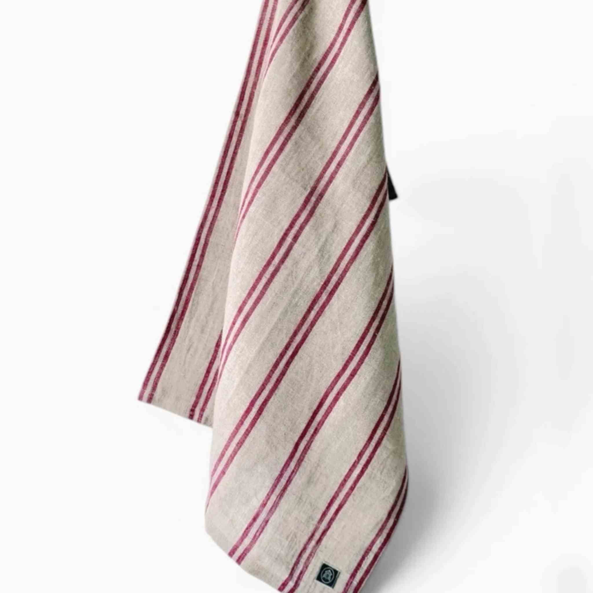 A folded beige linen tea towel with diagonal dark red stripes, hanging against a clean white background.