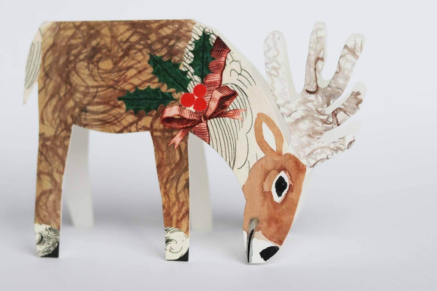 Decorative reindeer figure with a bow and holly leaves on a white background