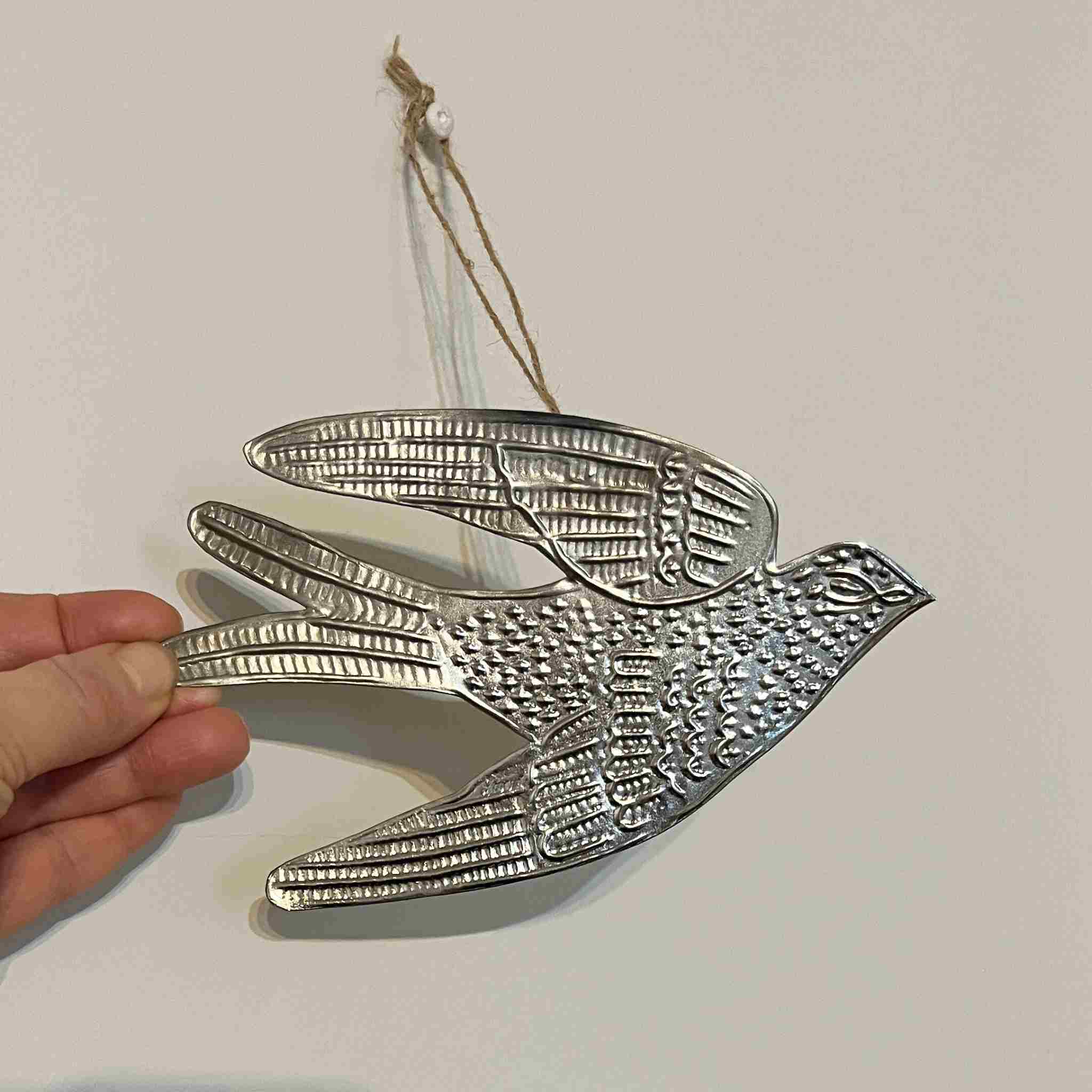 Decorative metal bird ornament held by a hand against a plain background