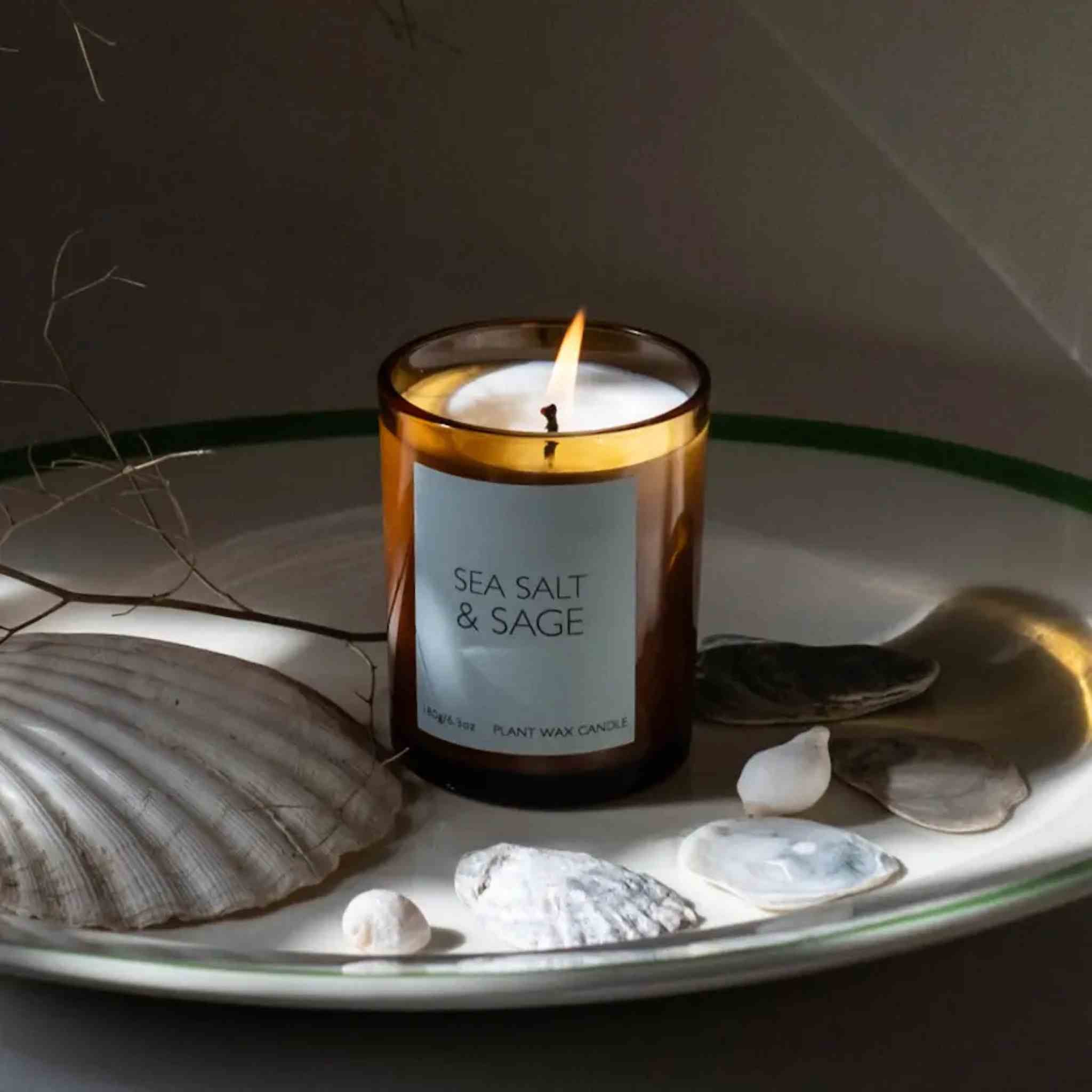 Candle labeled 'Sea Salt & Sage' on a plate with seashells