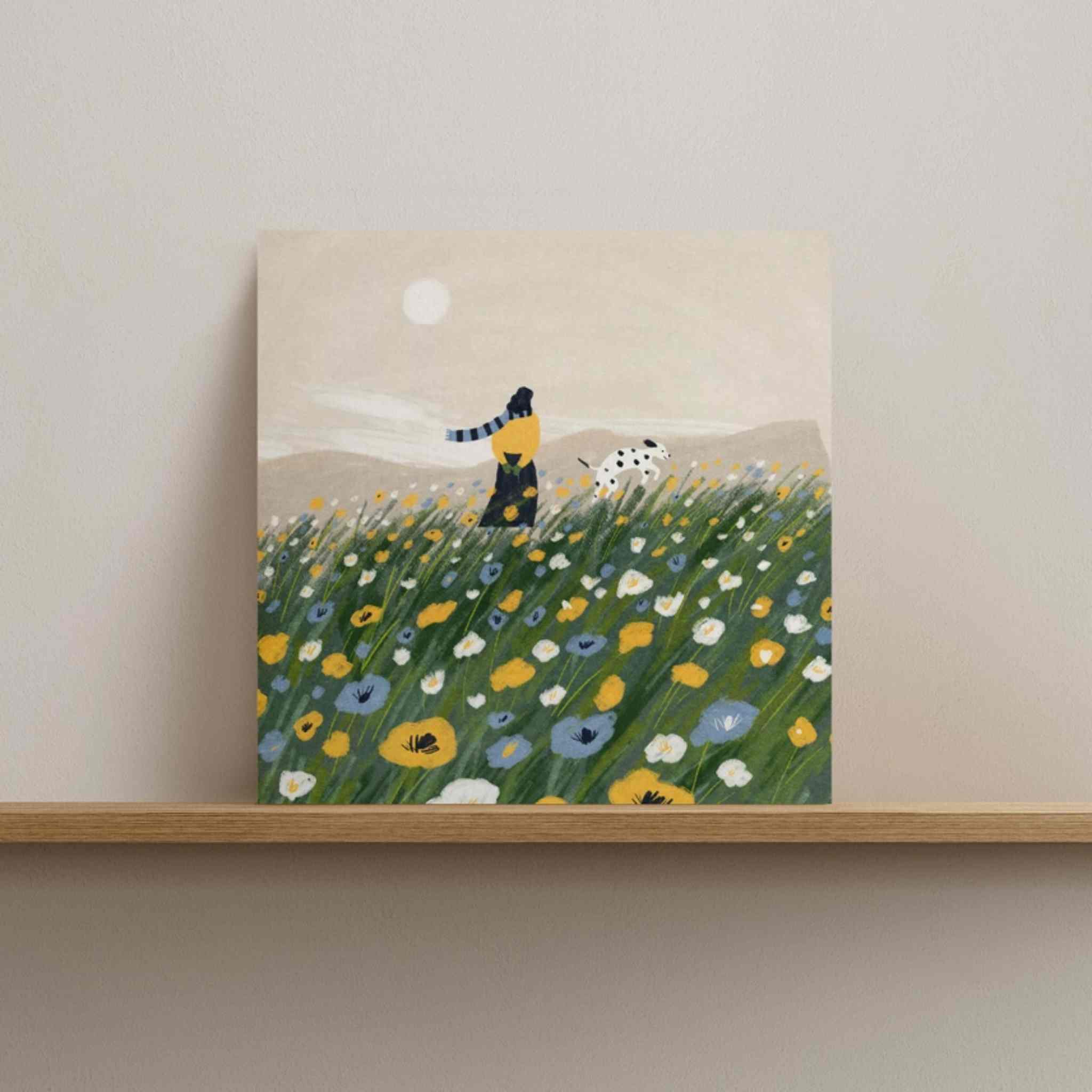 Framed artwork of a person and dog in a field with flowers on a shelf.