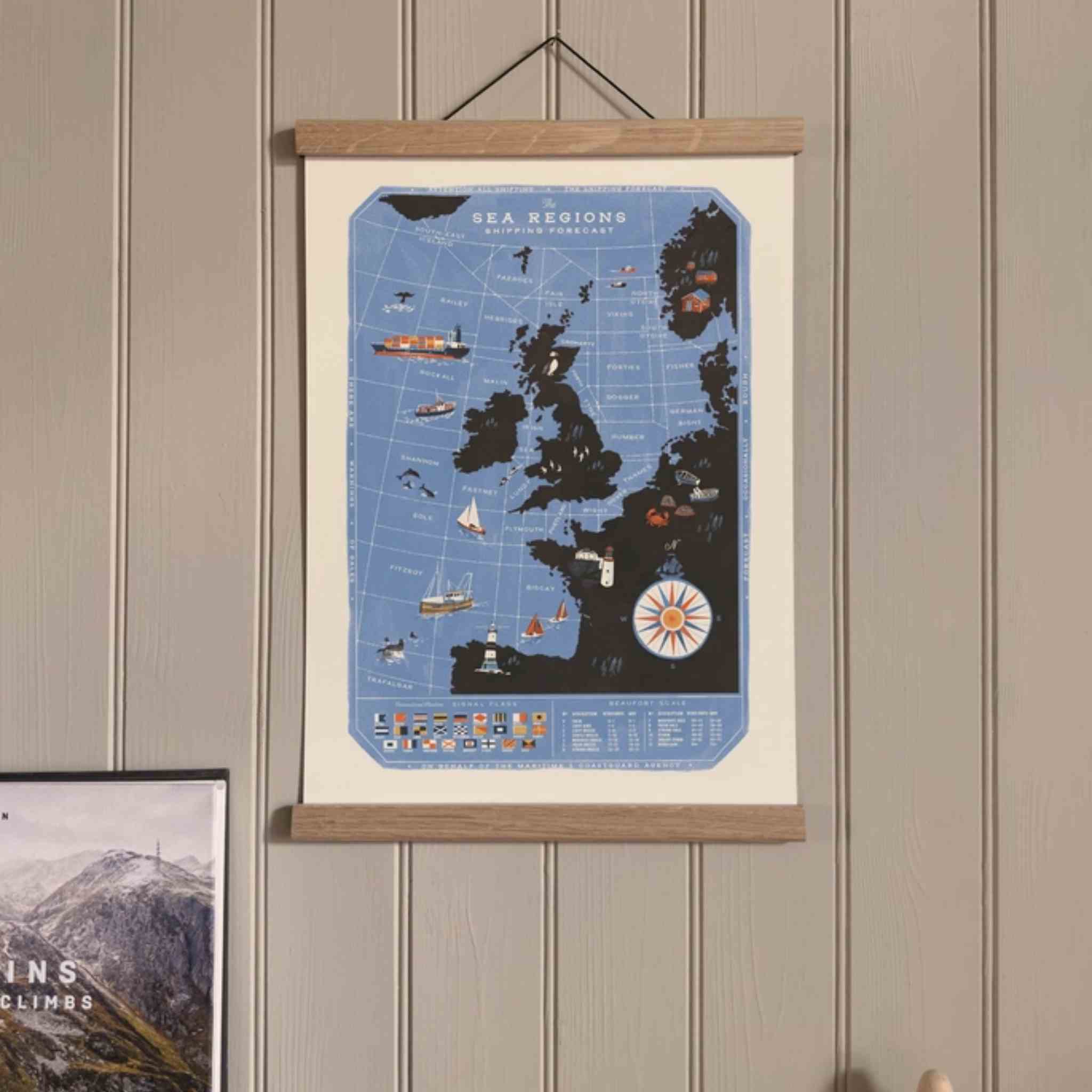 A hanging wall poster showing a stylized blue map of the UK and Ireland with illustrated ships and boats, mounted in a light wood frame on a beige paneled wall.