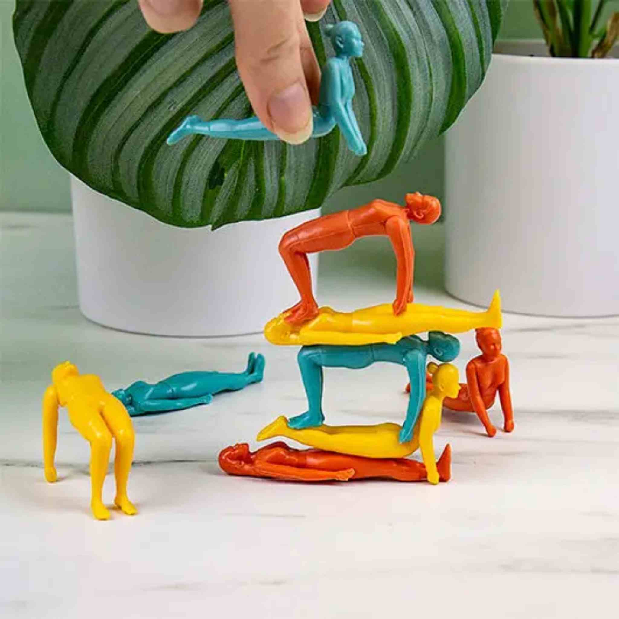 Colorful plastic figures stacked on top of each other with a hand placing a blue figure on top.