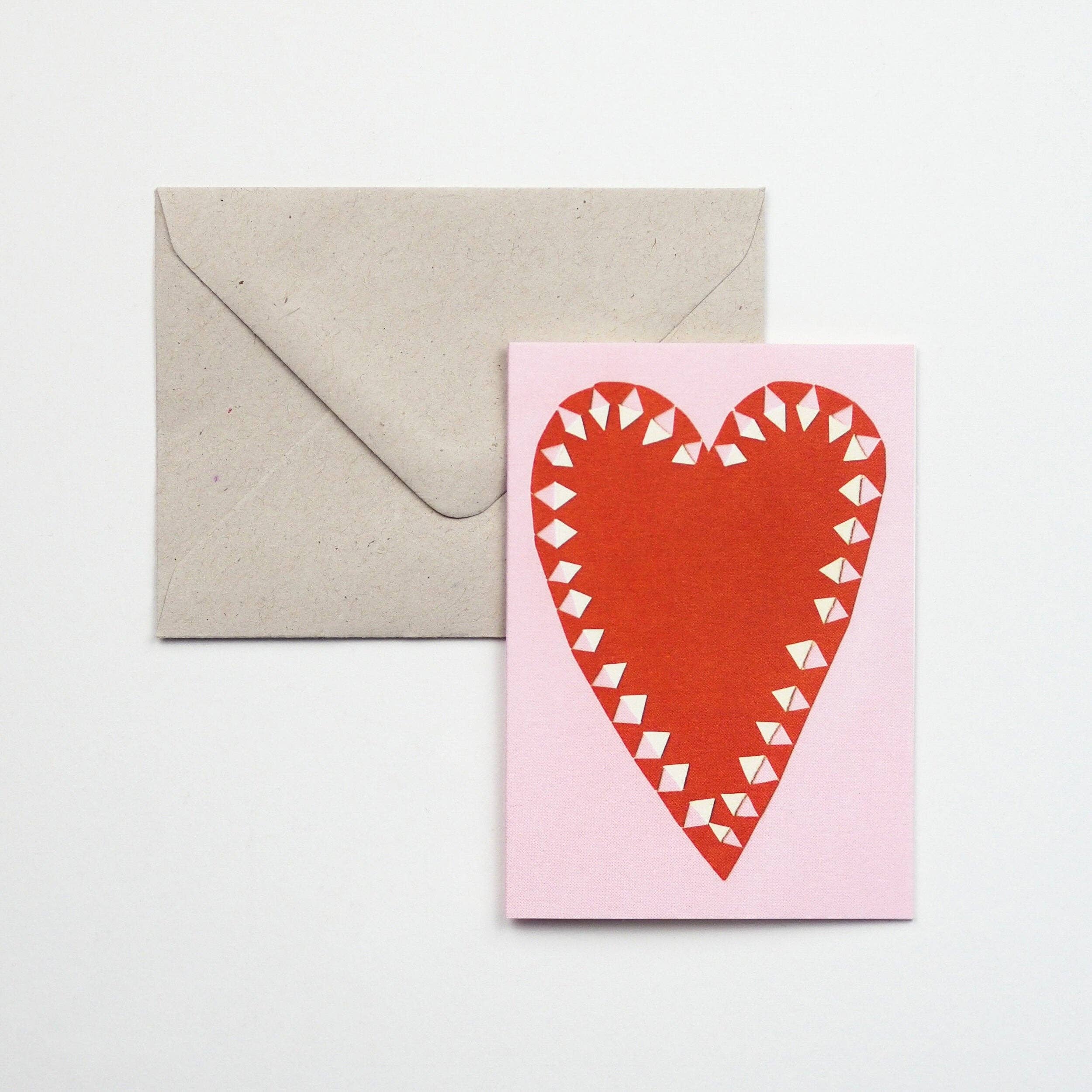 Card with red heart design on pink background and beige envelope