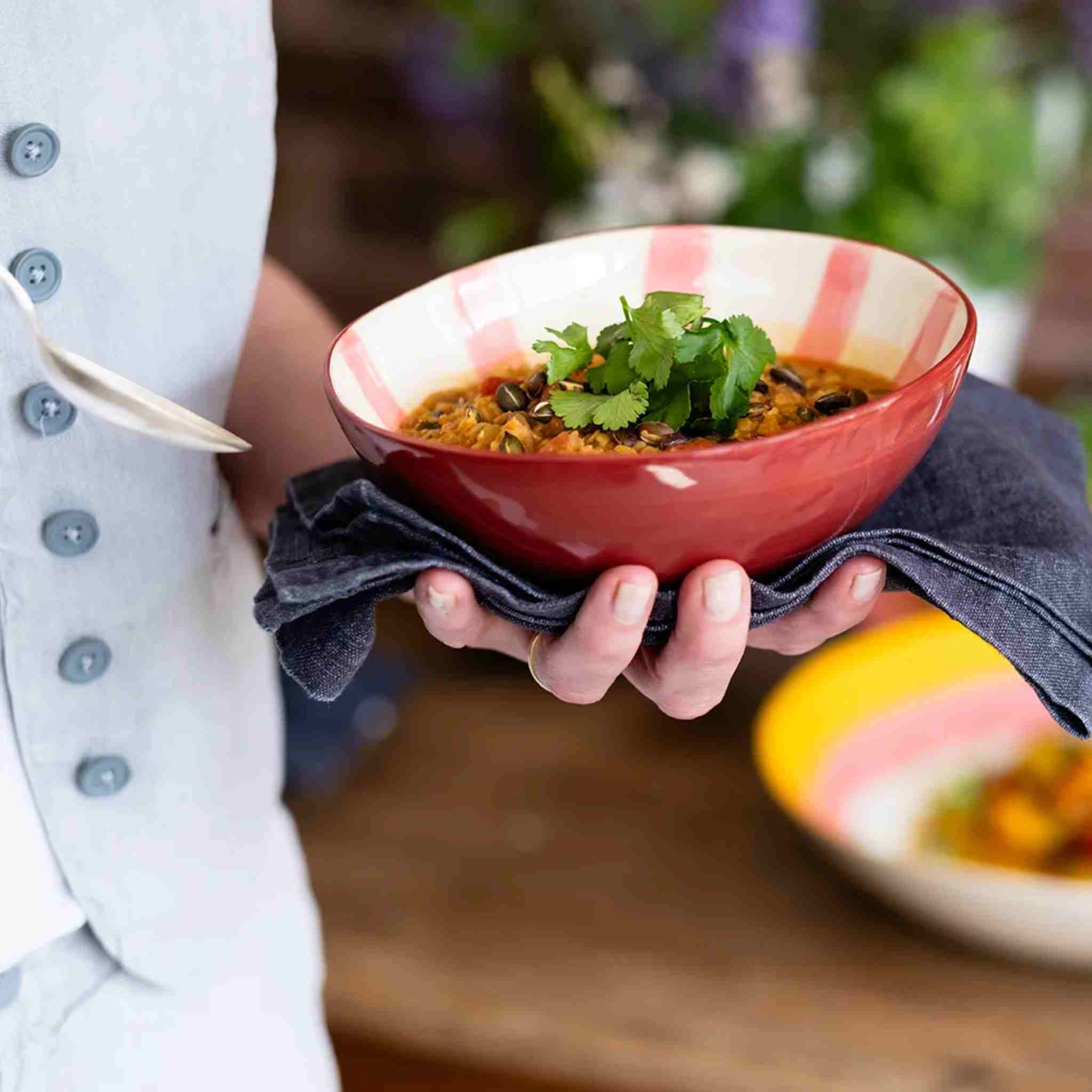 Person holding a red bowl of food with a blurred outdoor background