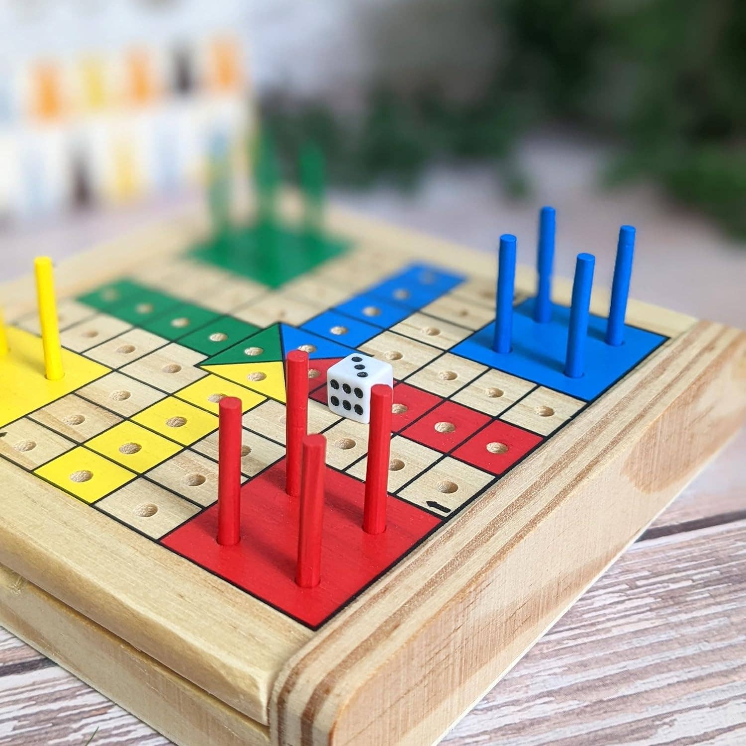 Wooden Ludo board game with colorful pegs and a dice on a wooden surface.