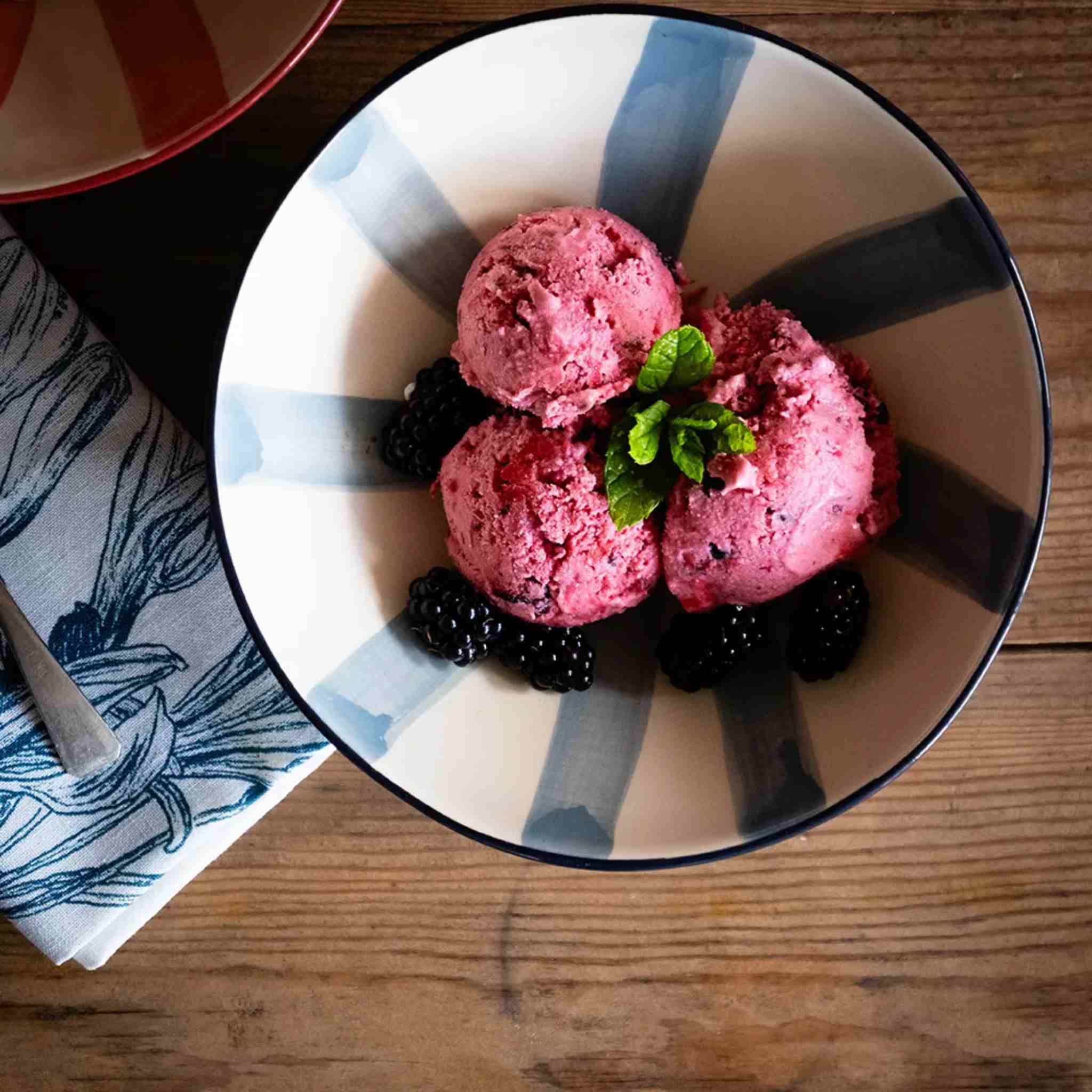 Pink ice cream with blackberries and mint leaves on a striped bowl