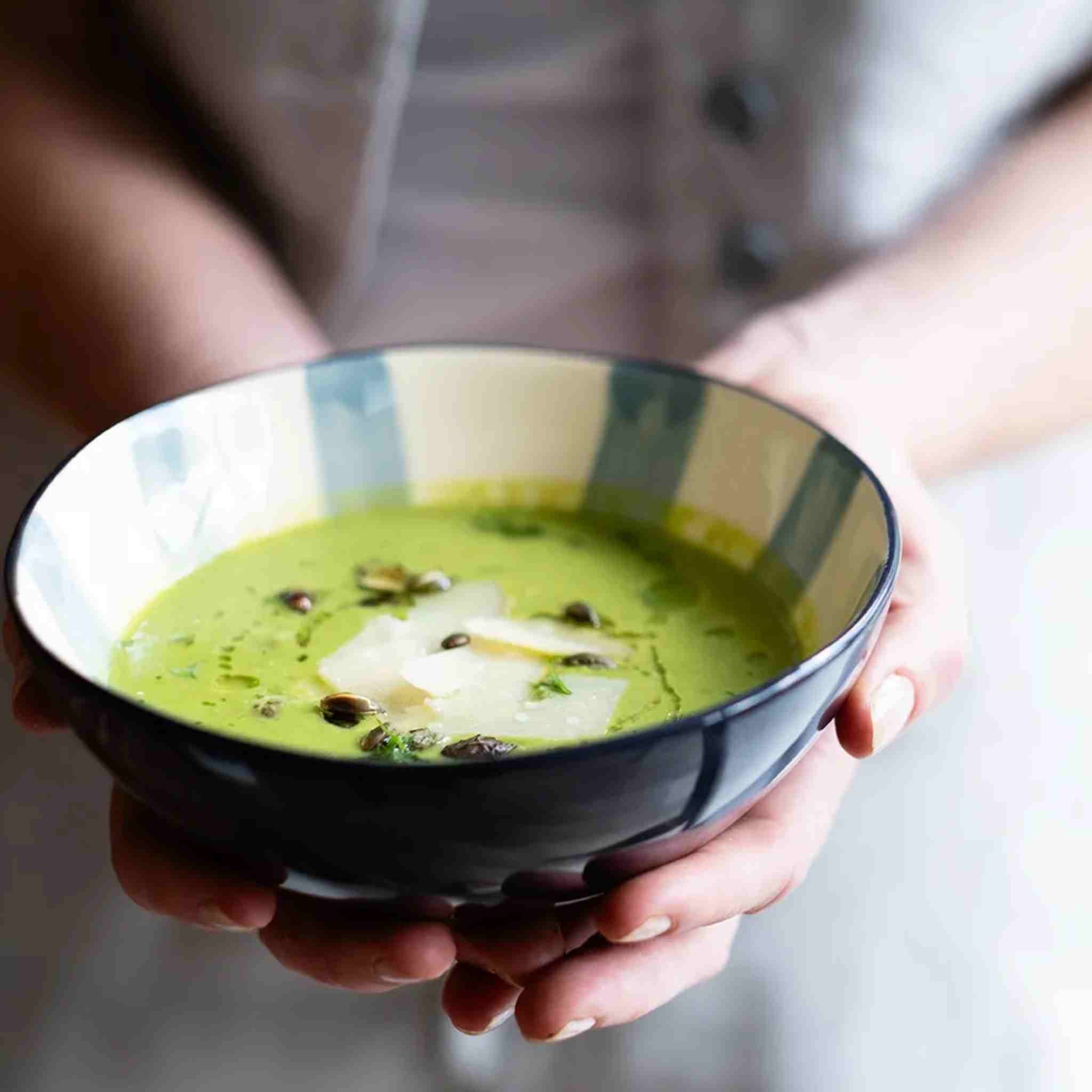 Person holding a bowl of green soup with a blurred background
