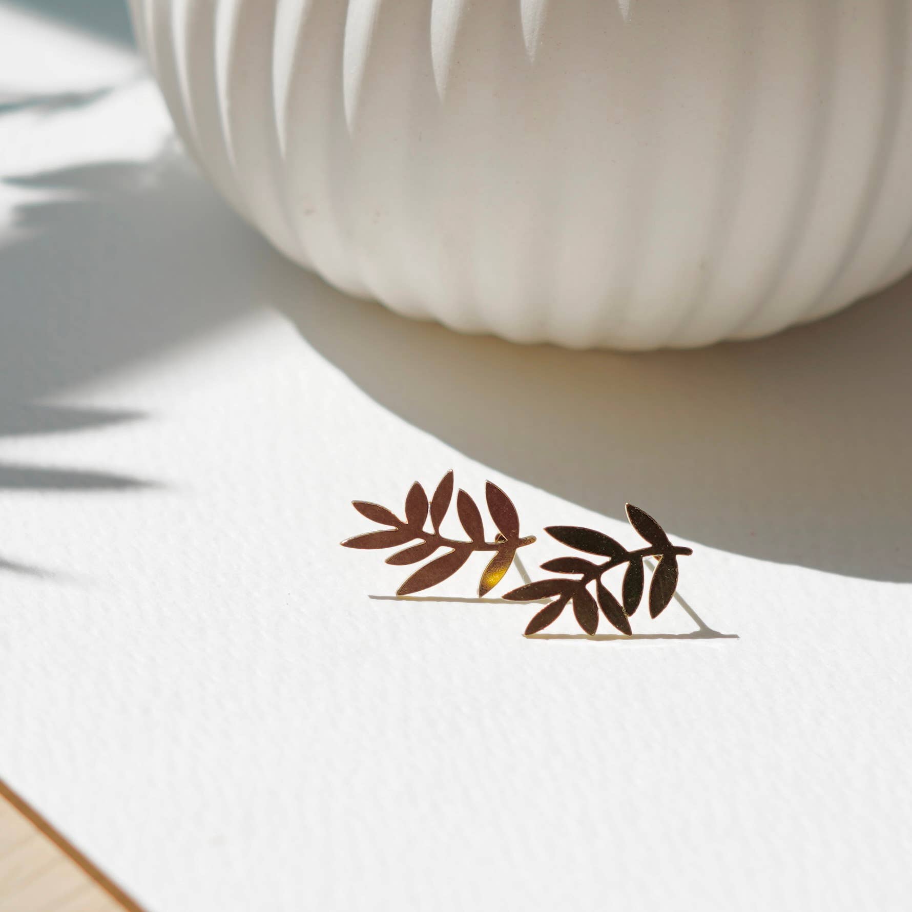 Pair of leaf-shaped earrings on a white surface with a blurred background